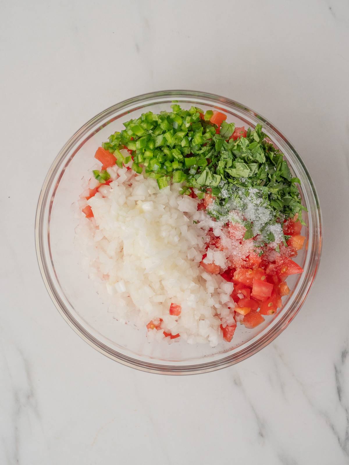 A glass mixing bowl with all the ingredients to make pico de gallo.