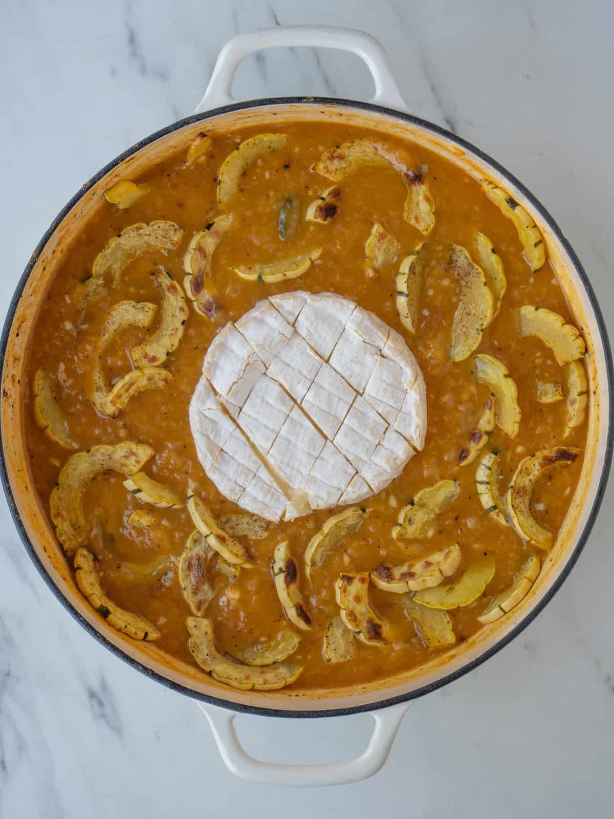 A braiser with squash risotto being cooked, with roasted delicata squash added, and camembert set in the center.