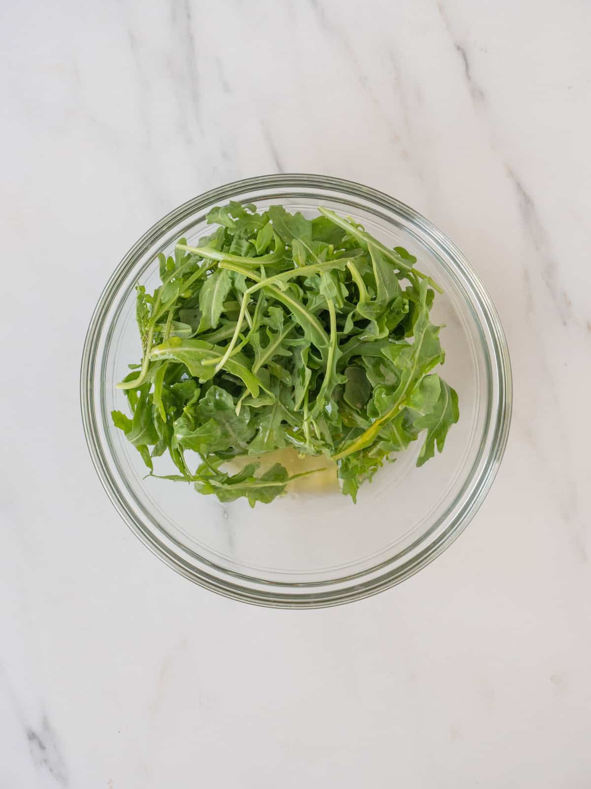 A bowl with wild arugula, lemon juice and olive oil combined to make a  