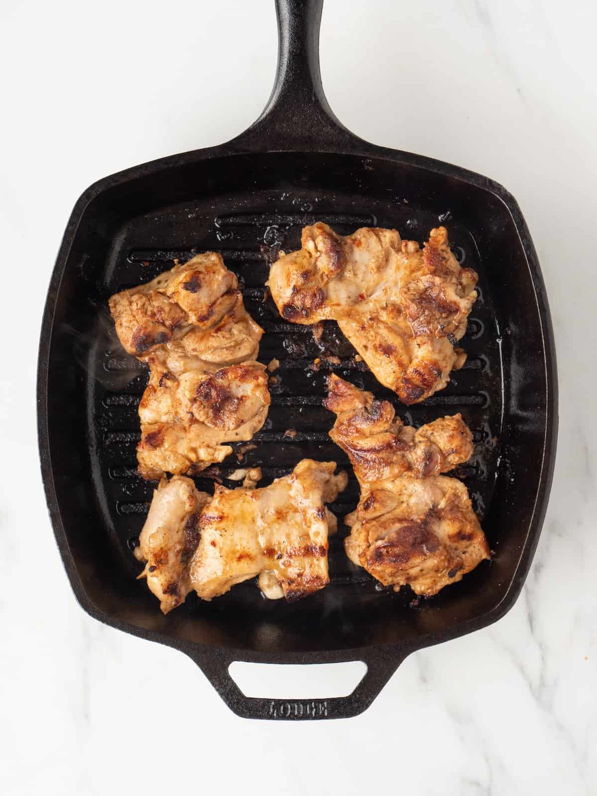 A rectangular skillet with chicken thighs being grilled.