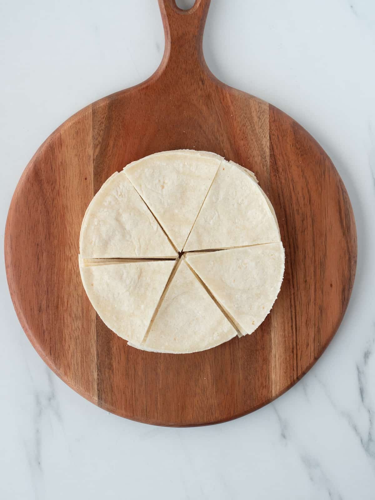 A wooden board with stack of tortillas, cut into ⅙th triangle pieces.