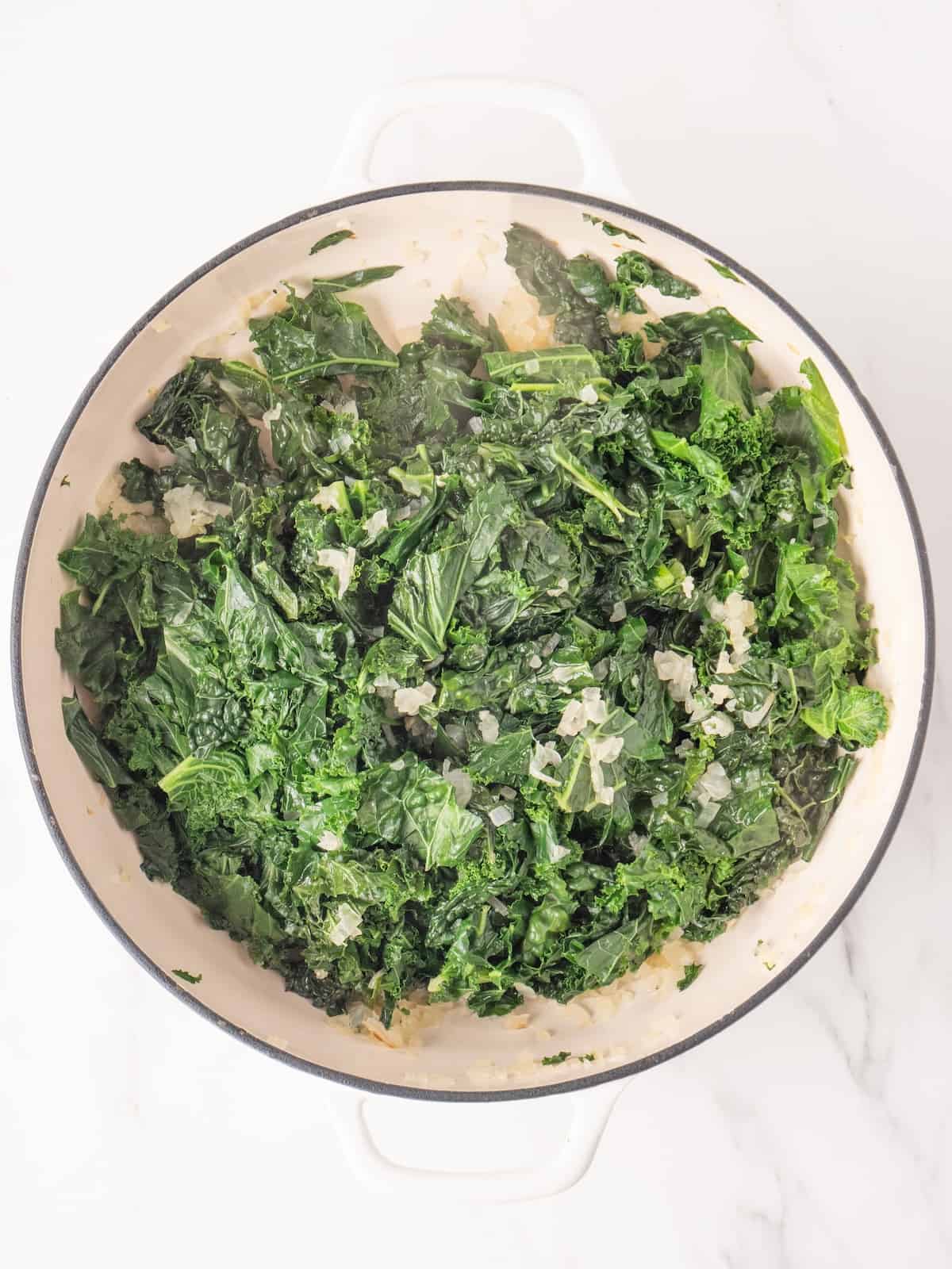A large white dutch oven with chopped kale being cooked.
