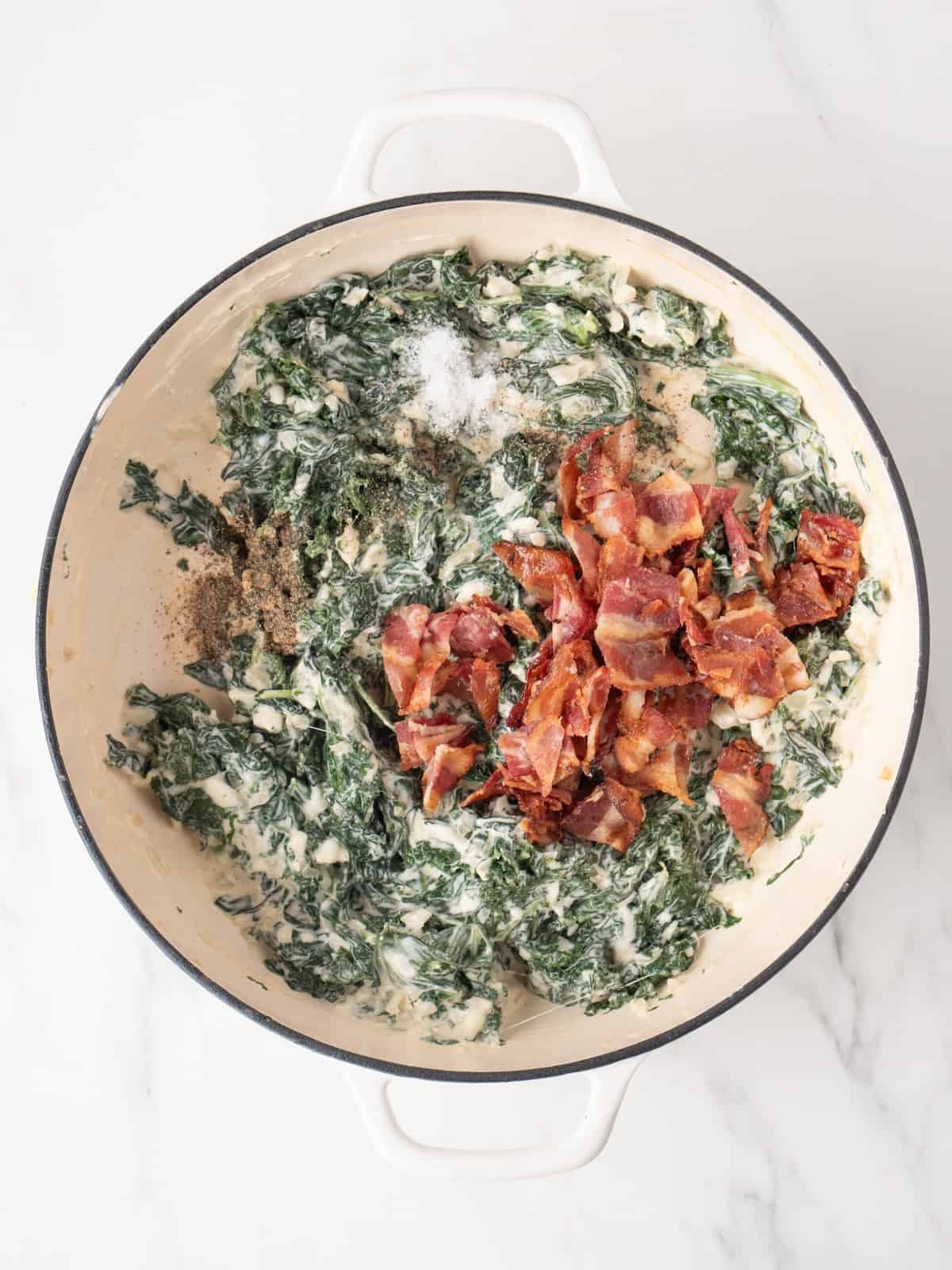 A large white dutch oven with kale dip mixture, and cooked bacon bits just added.