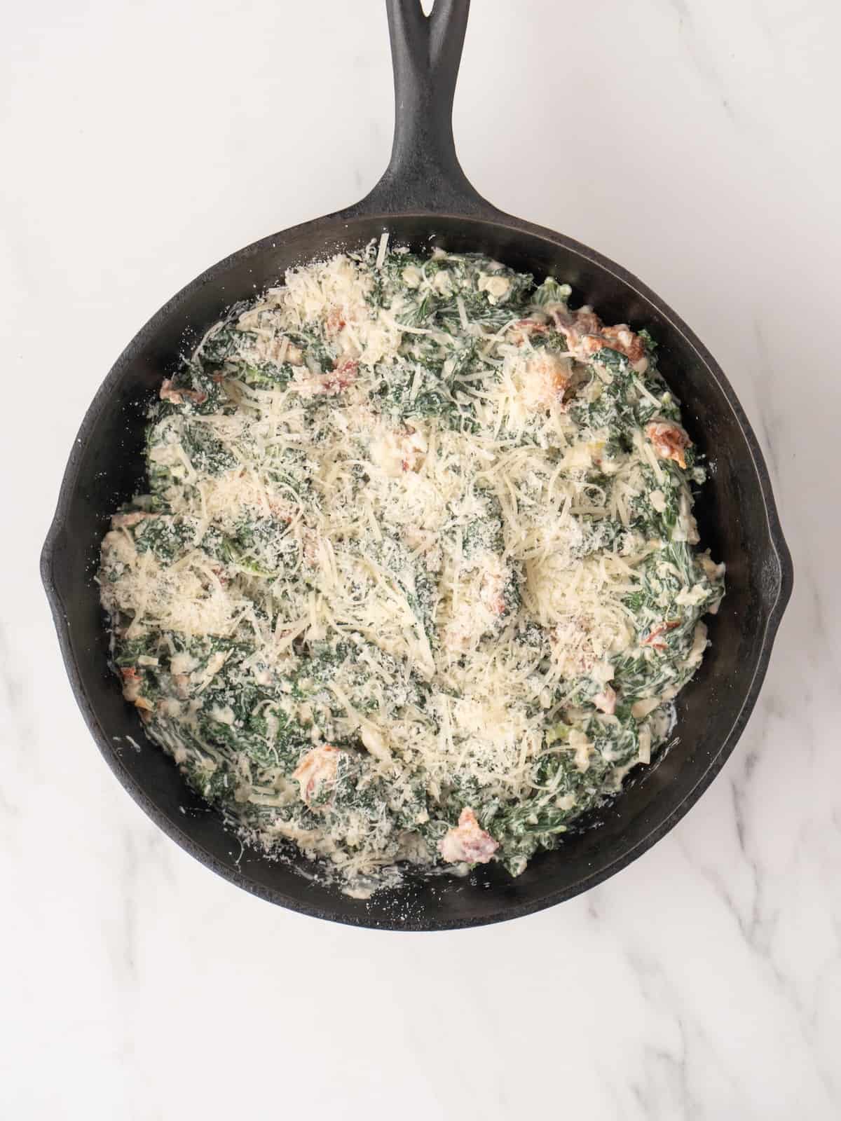 A skillet with hot kale and bacon dip topped with parmesan cheese.