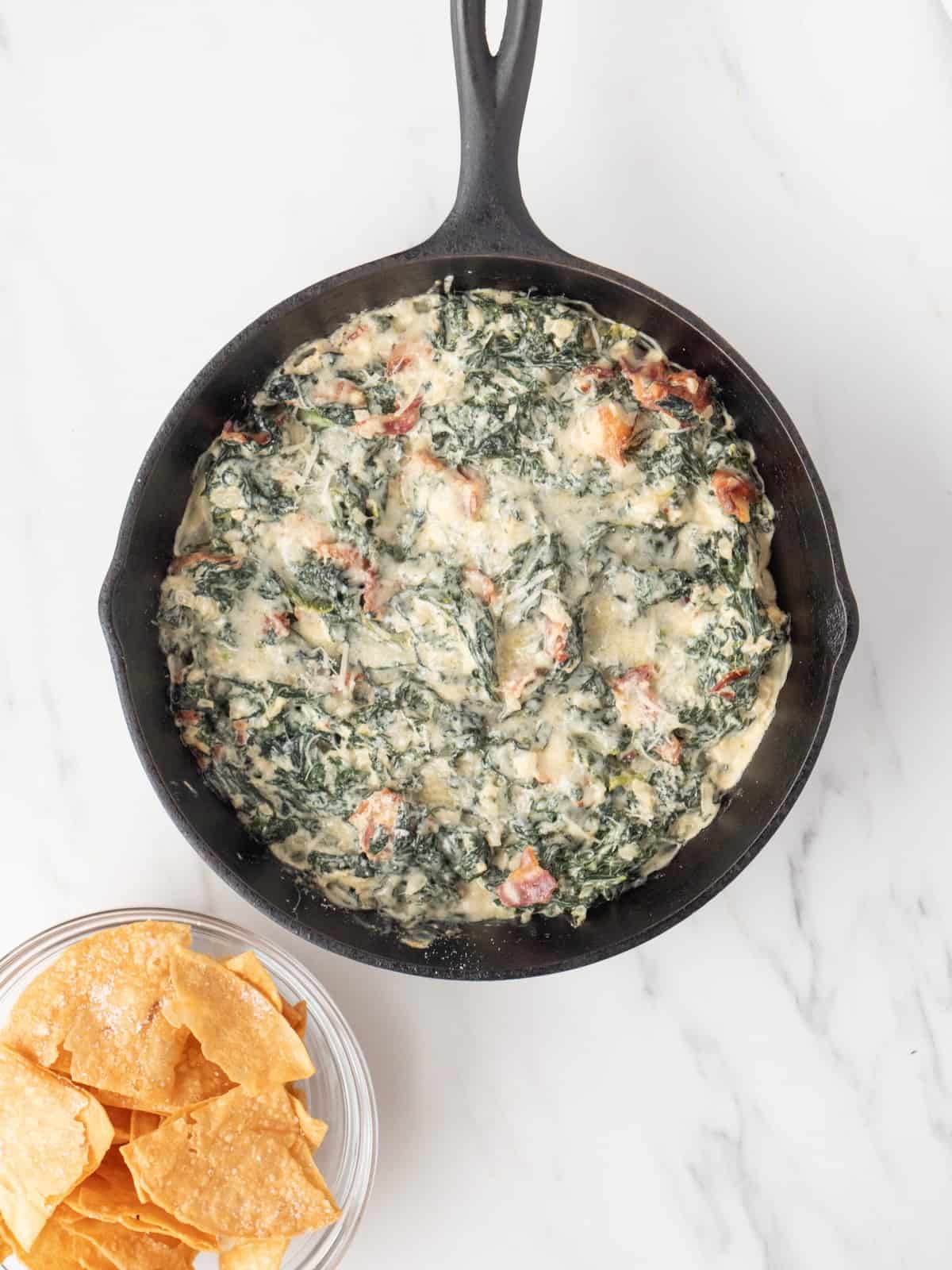 A skillet with hot kale and bacon dip topped with parmesan cheese melted in the oven.
