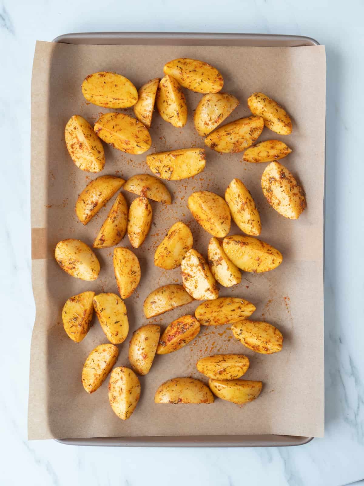 A parchment-lined baking sheet with quartered potatoes tossed in seasoning and oil.
