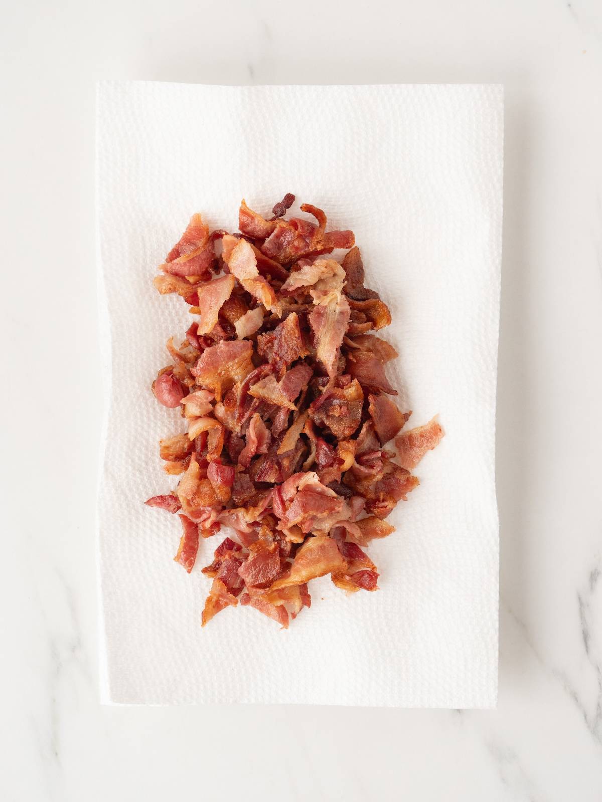 A paper towel-lined plate with cooked bacon.