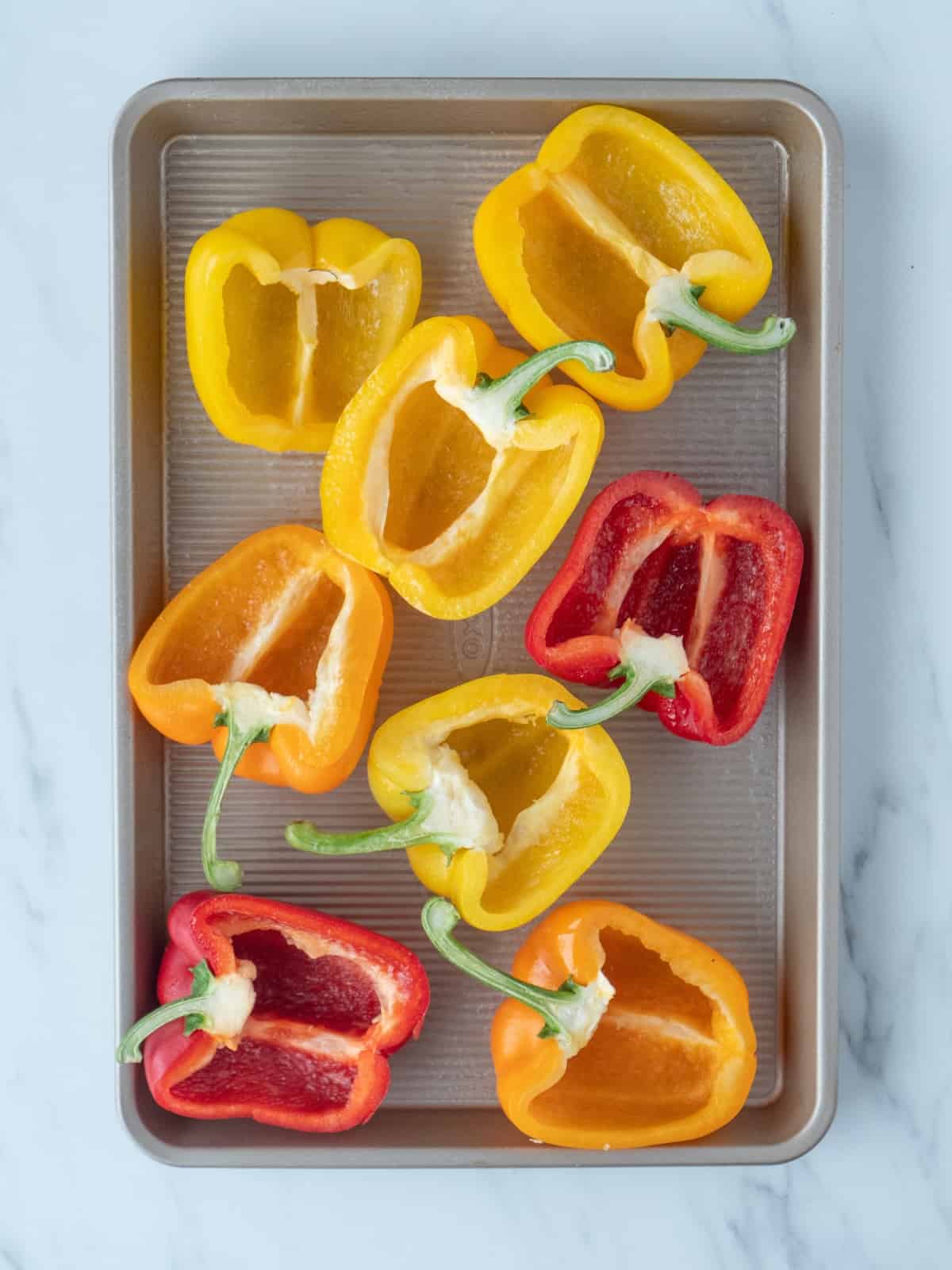 A rectangular baking sheet with halved bell peppers of various colors.