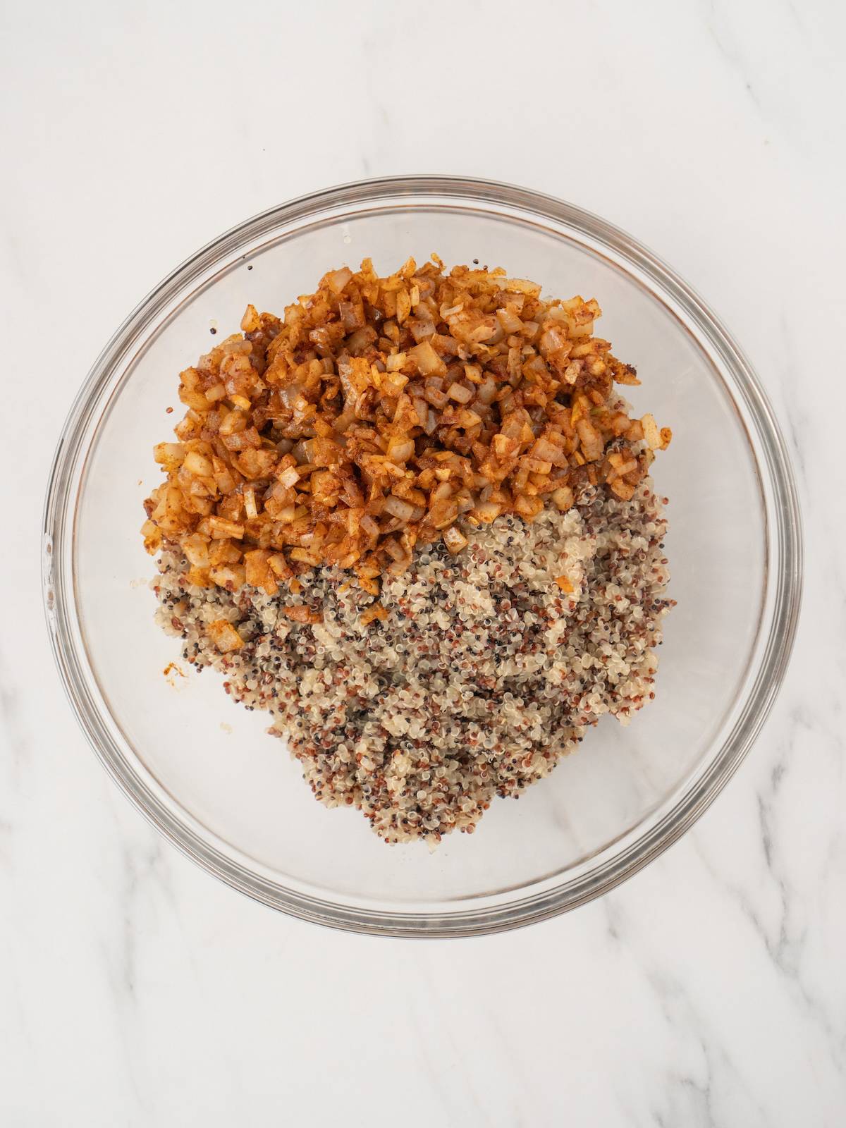A large glass mixing bowl with cooked quinoa and seasoned sautéed onions.