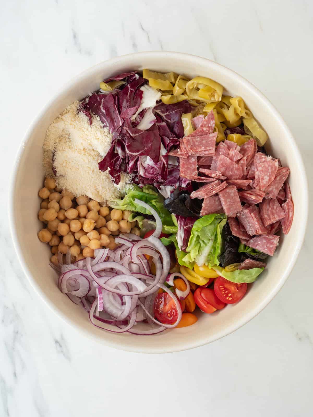 A bowl with a radicchio salad with red onion, little gem lettuce, radicchio, cherry tomatoes, canned chickpeas, genoa salami and pepperoncini.