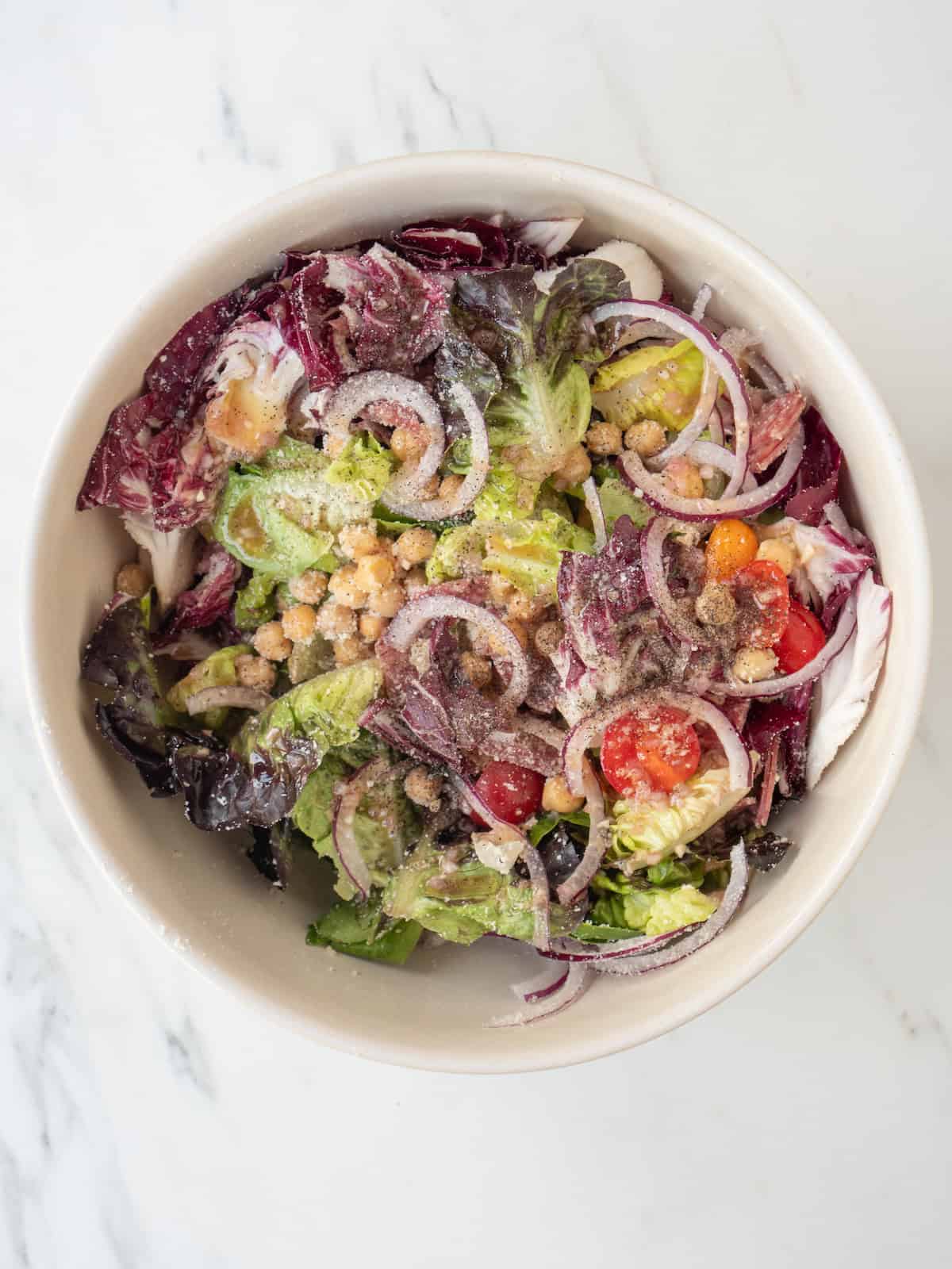 A bowl with radicchio salad with red wine vinaigrette added along with salt and pepper.