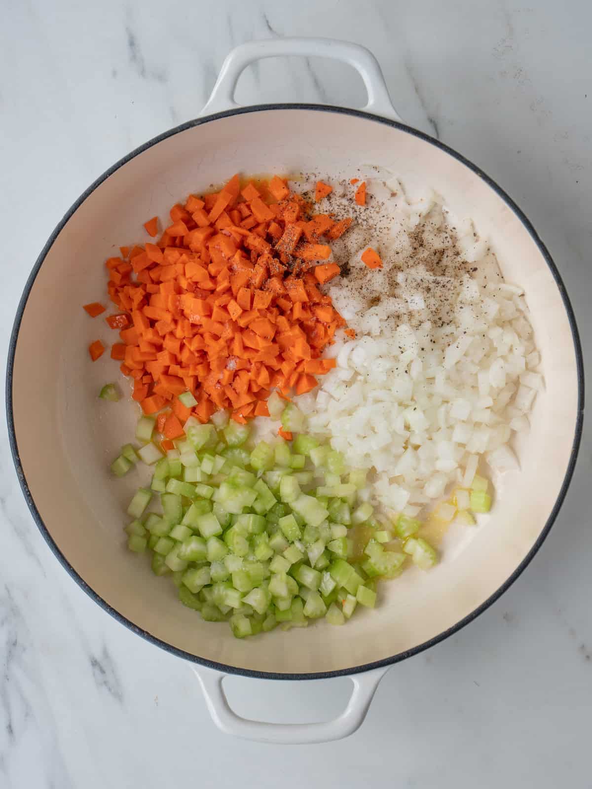 A dutch oven with diced onion, carrots and celery being sautéed.