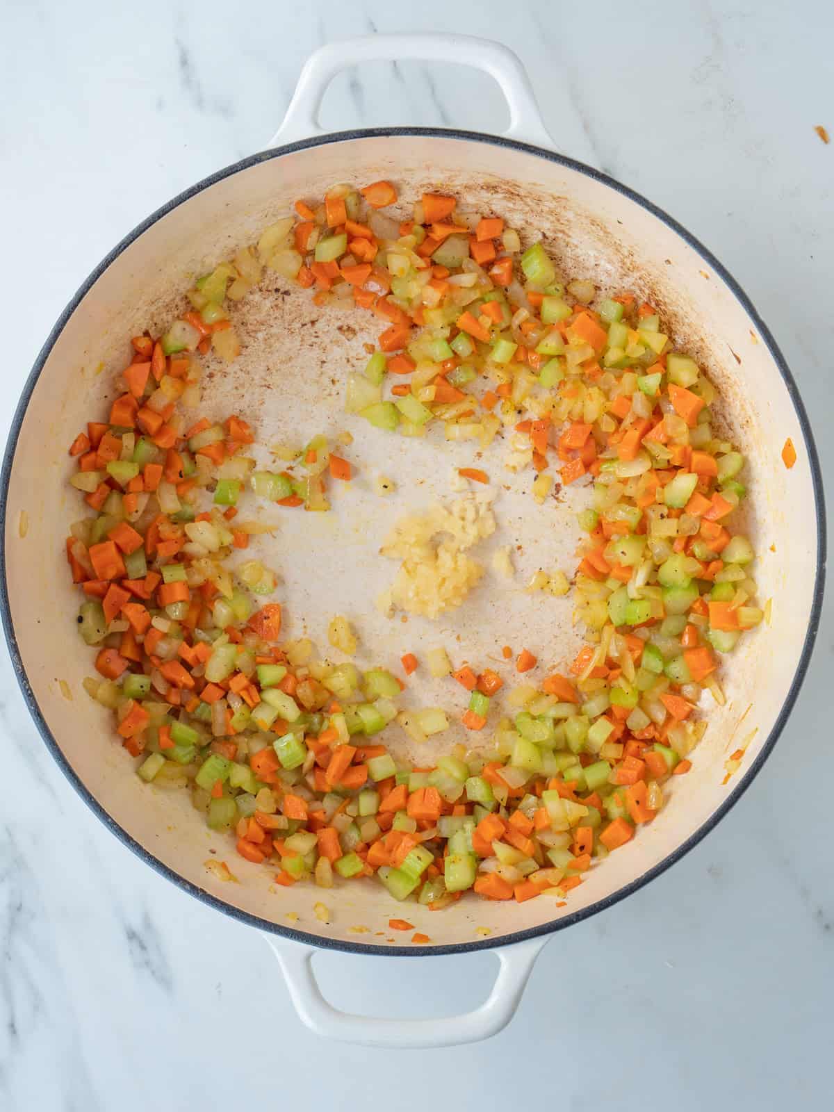 A dutch oven with diced onion, carrots and celery being sautéed and garlic added to it.