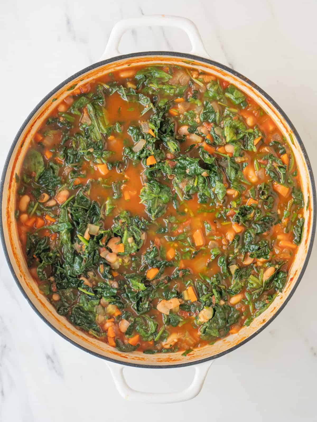 A dutch oven with ribollita soup being made, and wilted kale and spinach.