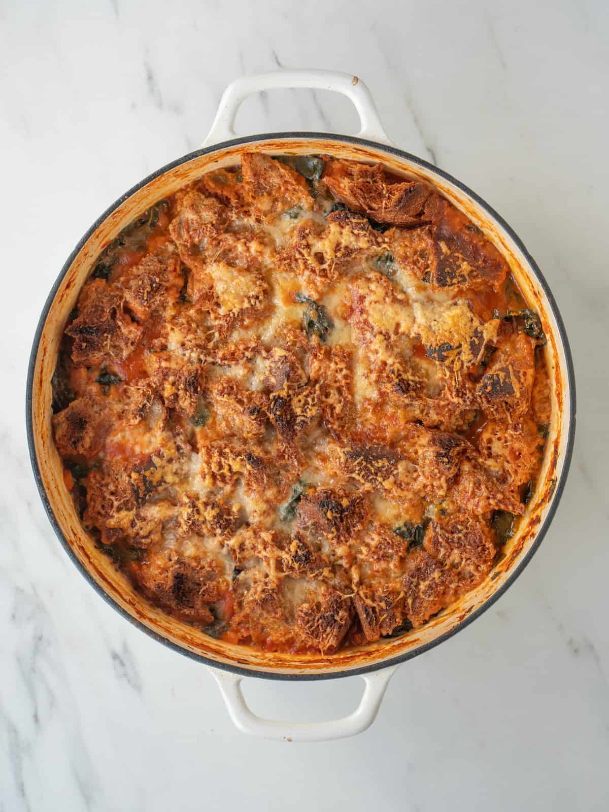 A dutch oven with ribollita soup made and fresh out of the oven, with crisped bread pieces and parmesan cheese on top.