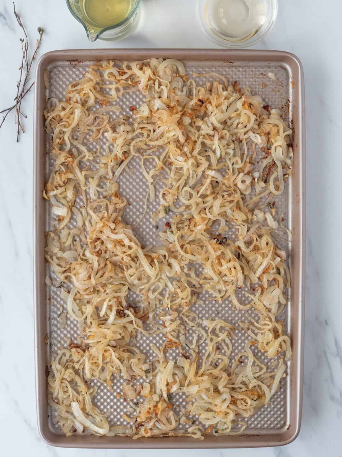 A baking sheet with partially roasted onions and shallots, and thyme sprigs removed from the sheet.
