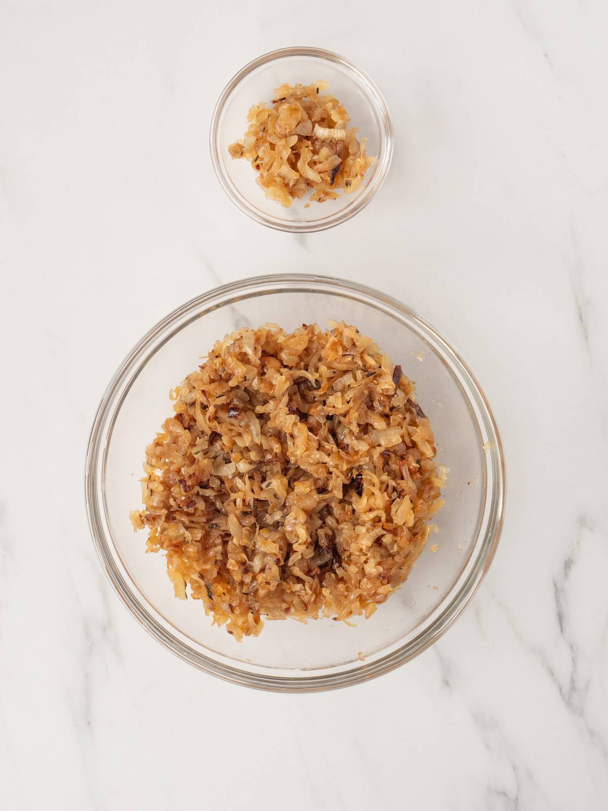A large glass mixing bowl and a small glass mixing bowl of roasted onions and shallots.