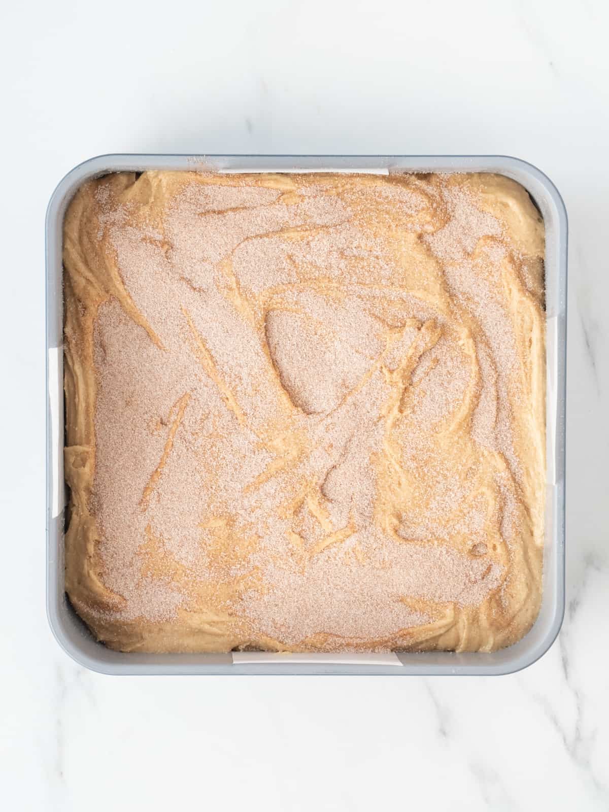 A 9x9 inch baking pan filled with snickerdoodle blondie brownie batter, sprinkled with cinnamon sugar.
