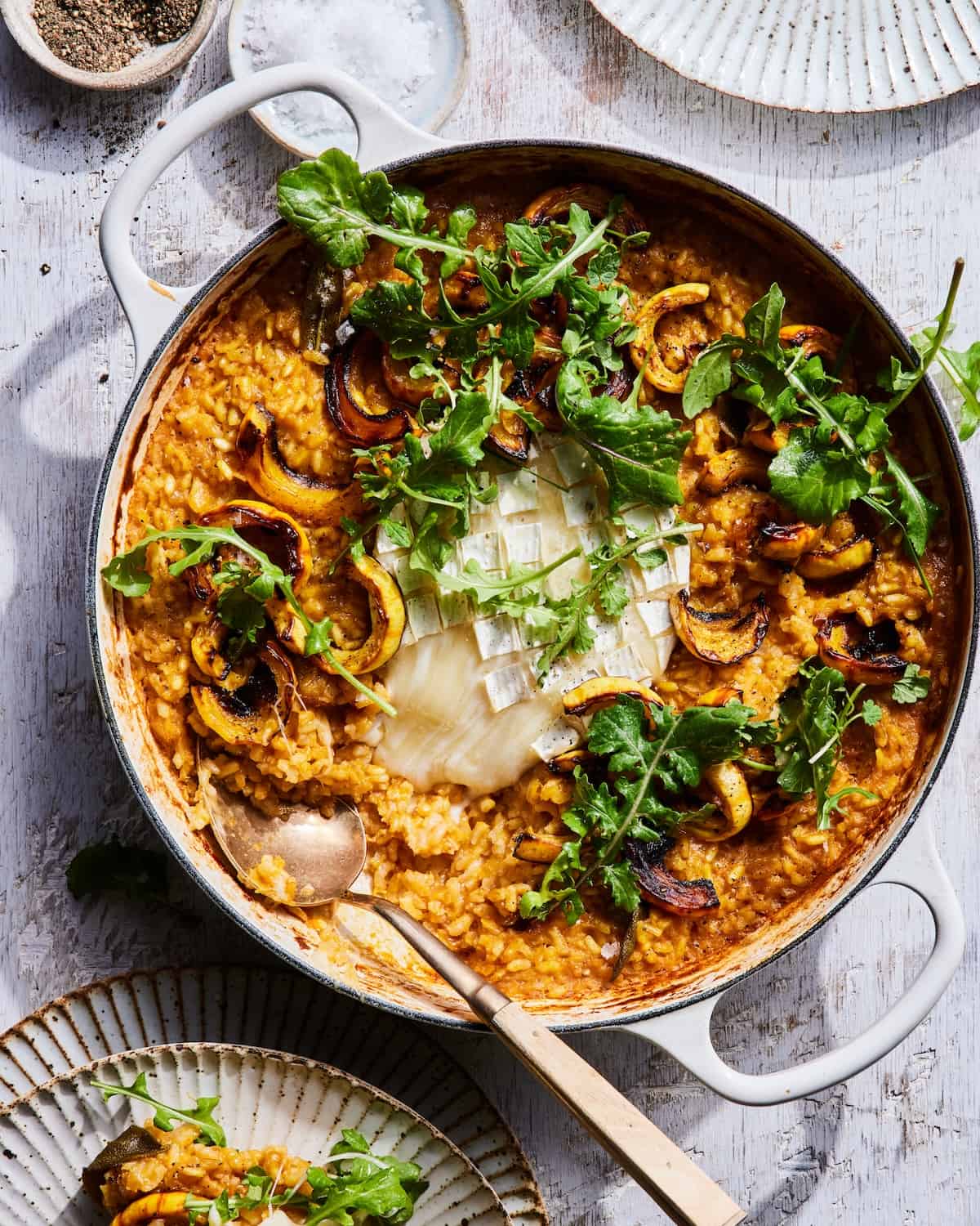Baked Squash Risotto in a low braiser with melted cheese in the center and dressed arugula 