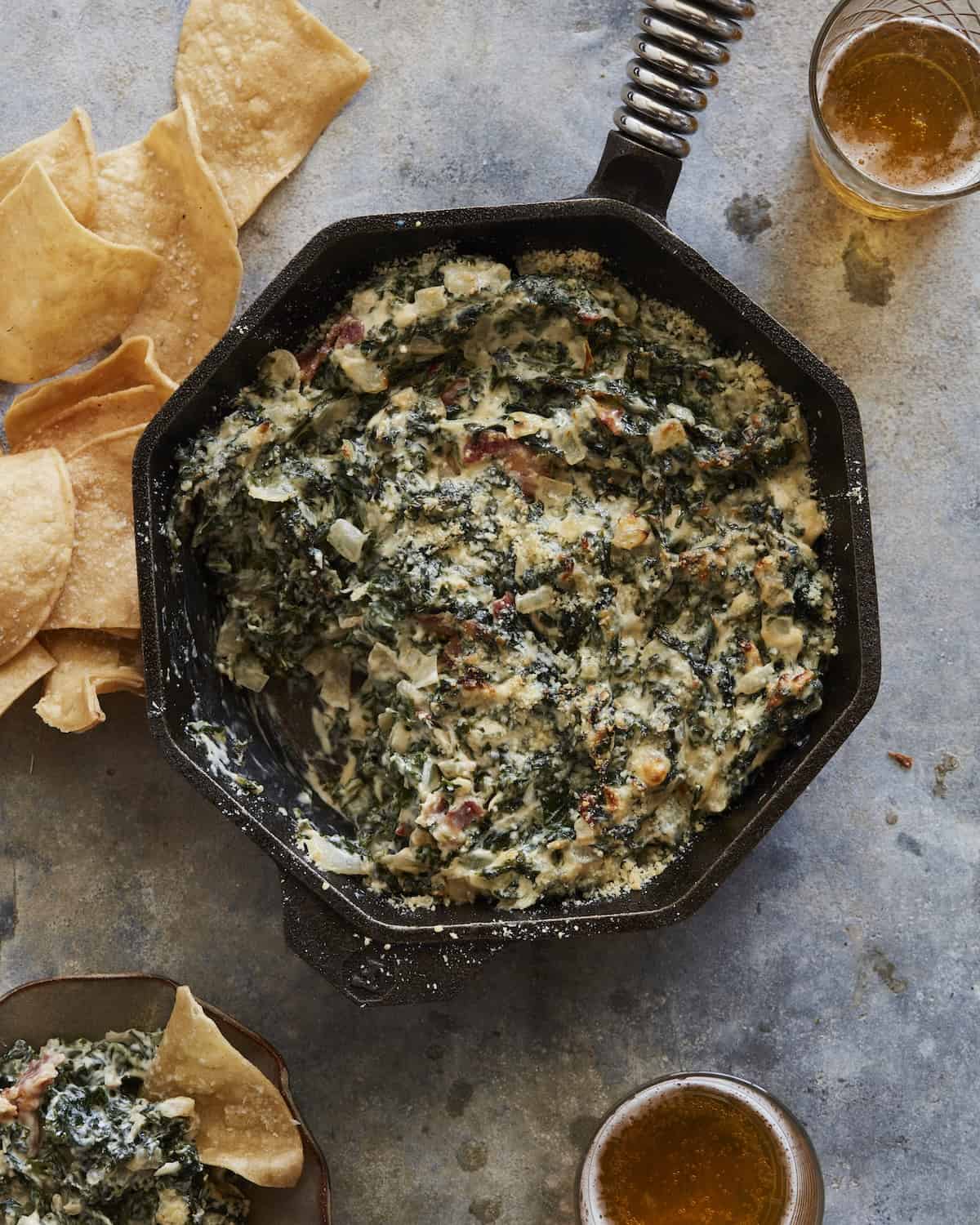 An octagon skillet with hot kale and bacon dip with some tortilla chips on the side.