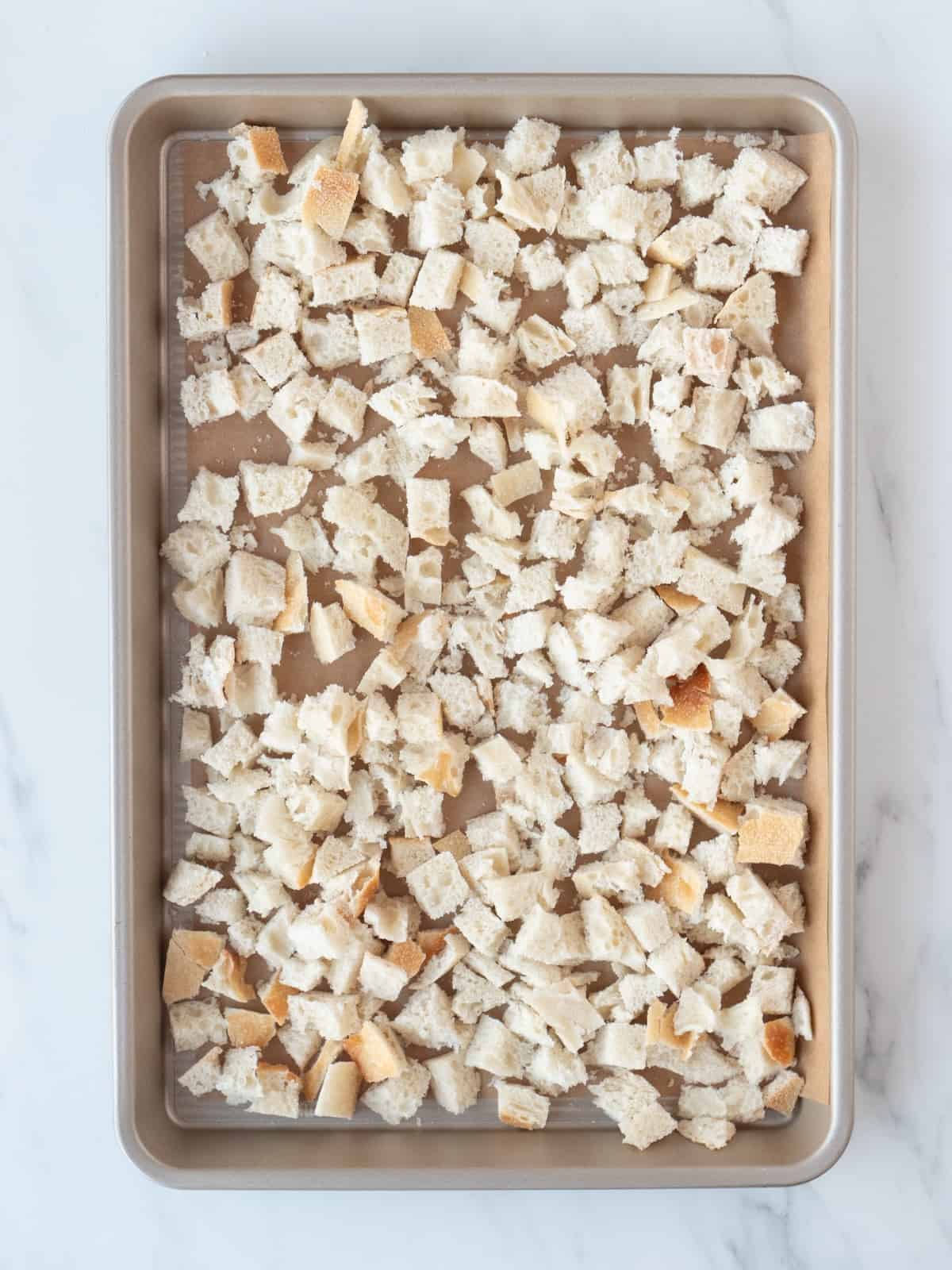 A rectangular parchment paper-lined baking sheet of cubed pieces of bread.