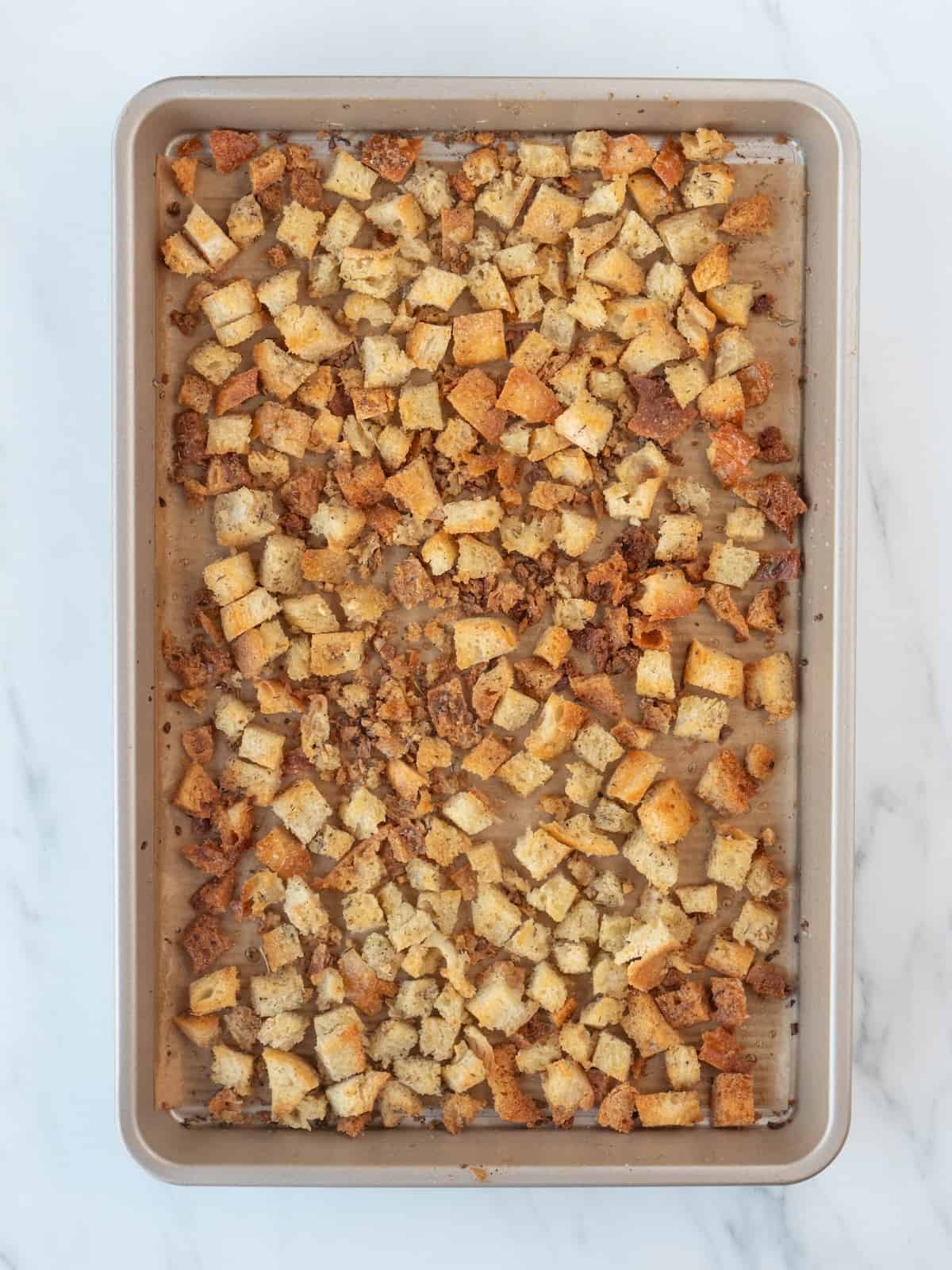 A rectangular parchment paper-lined baking sheet of cubed pieces of bread baked in the oven to make croutons.