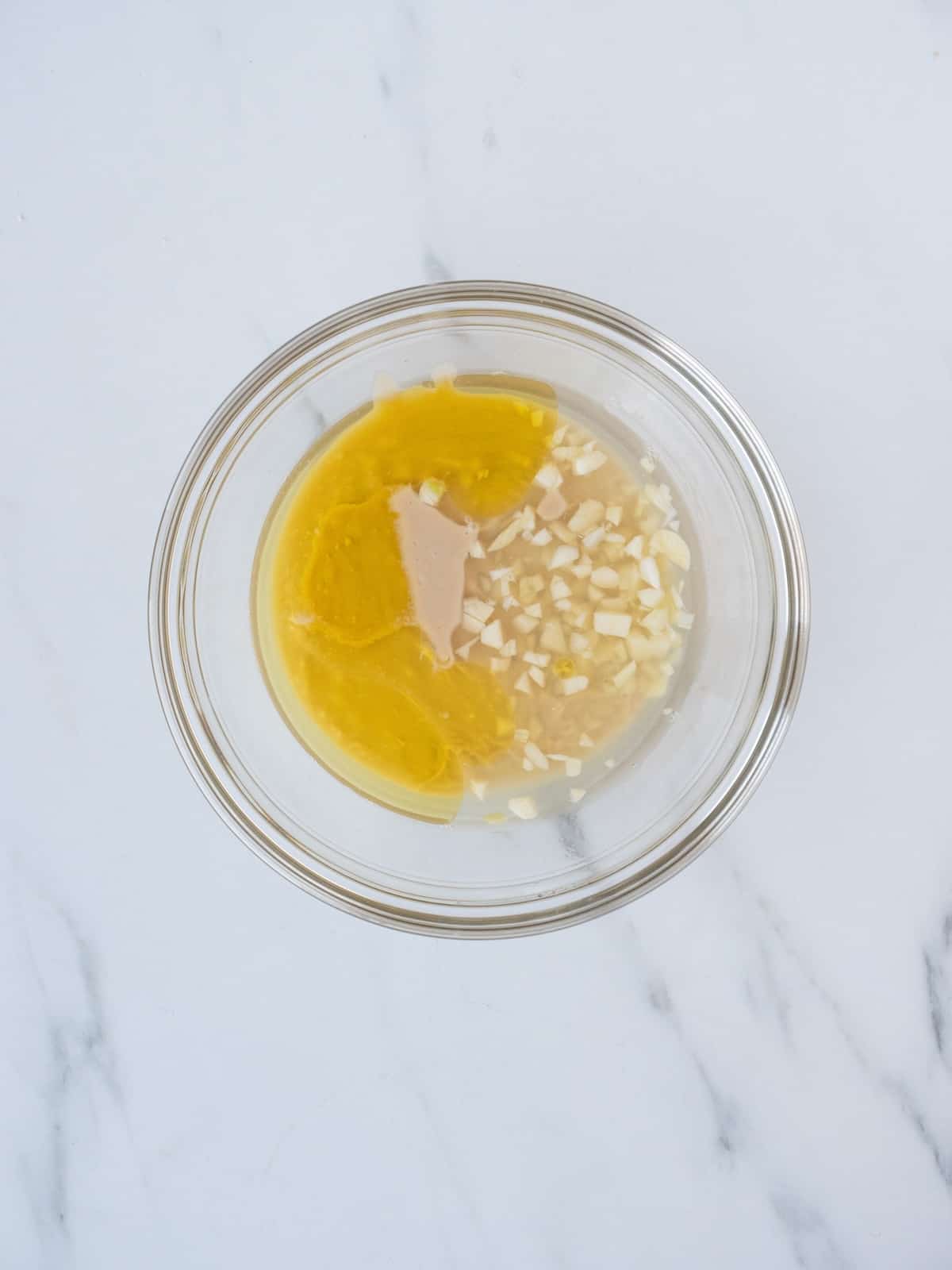 A small glass mixing bowl with tahini, lemon, oil and garlic.