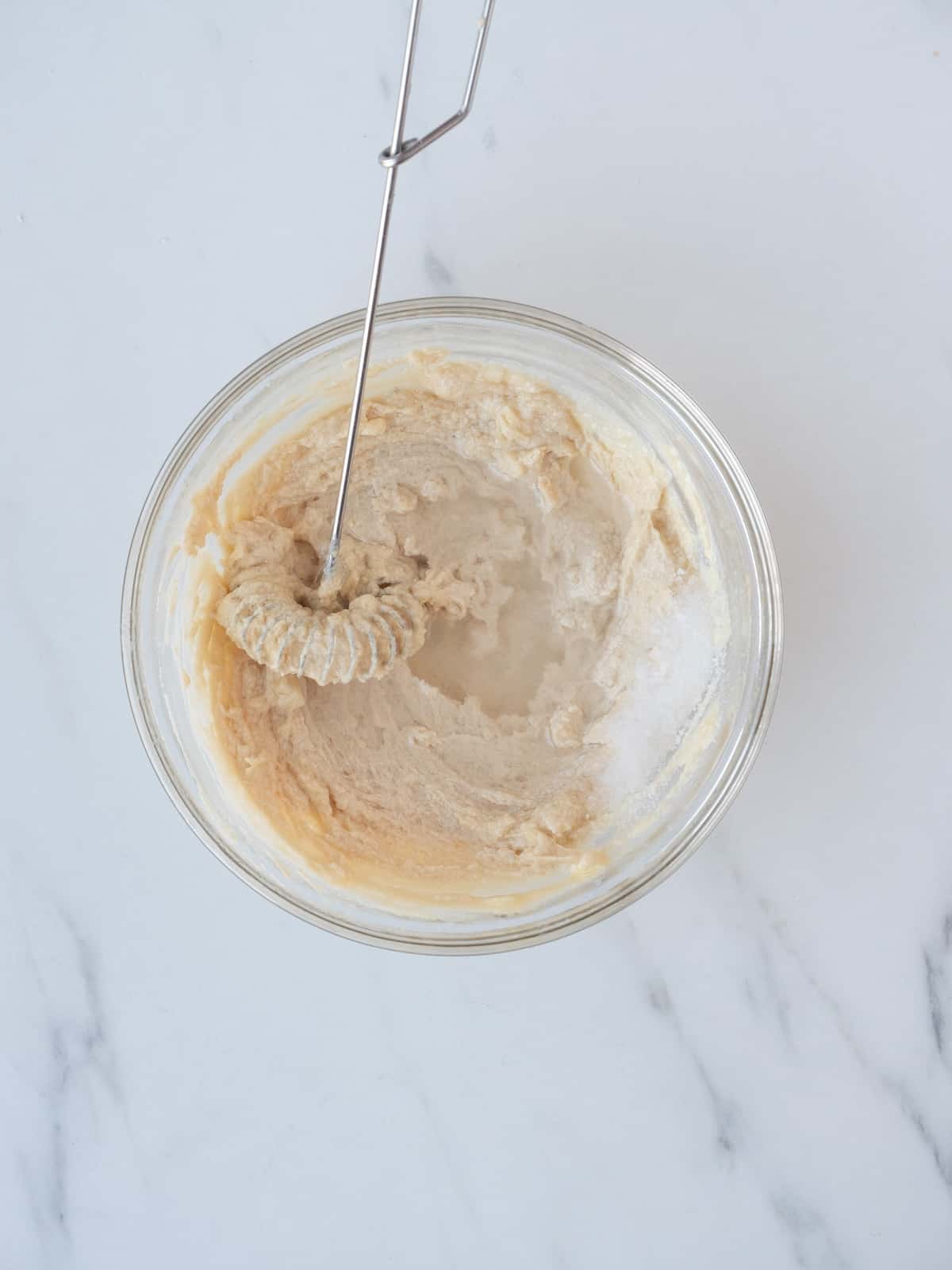 A small glass mixing bowl with tahini, lemon, oil and garlic, and a whisk being used to mix it into a dressing.