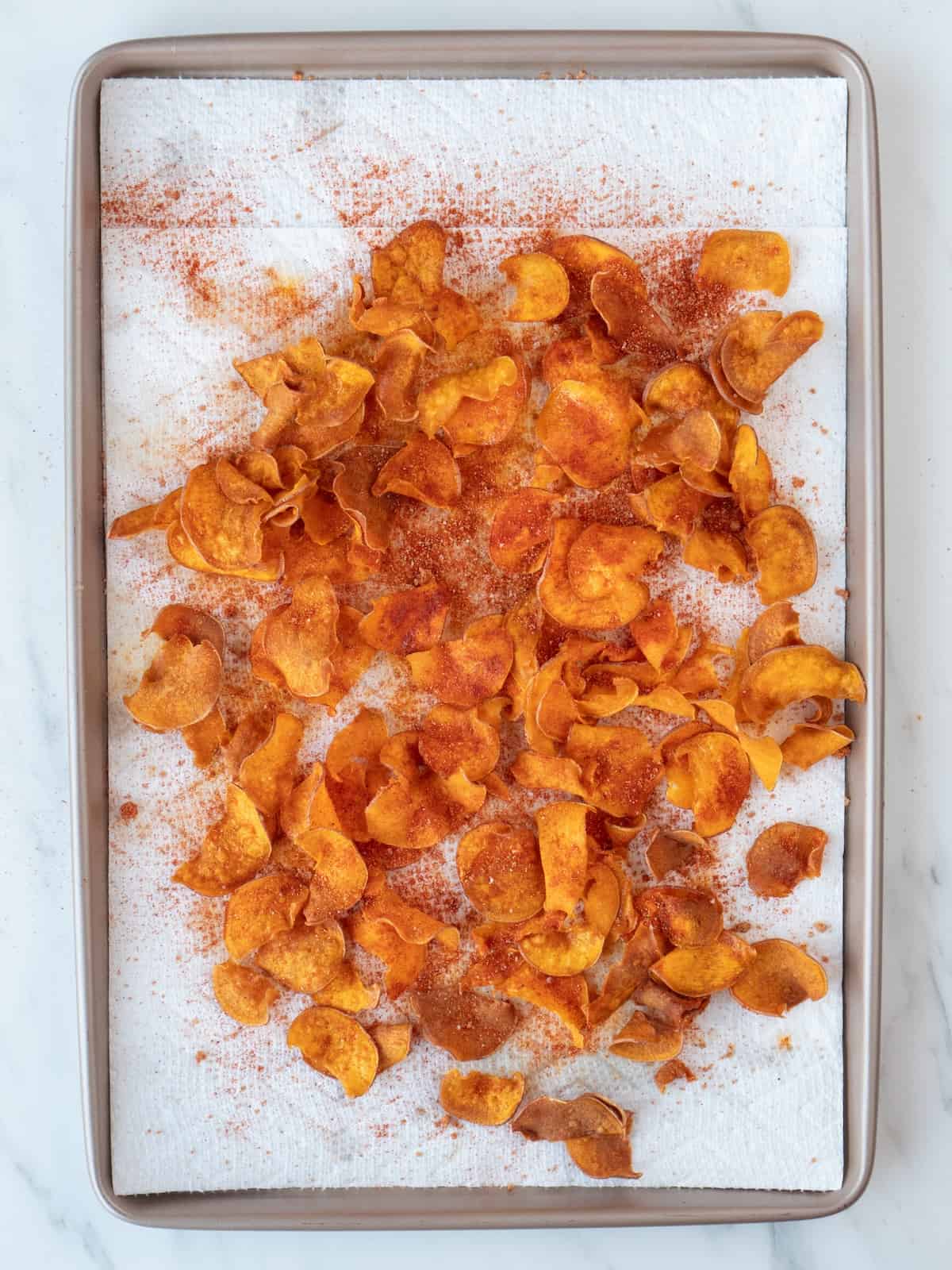 A paper tissue lined baking sheet with sweet potato chips dusted with BBQ spice mix.
