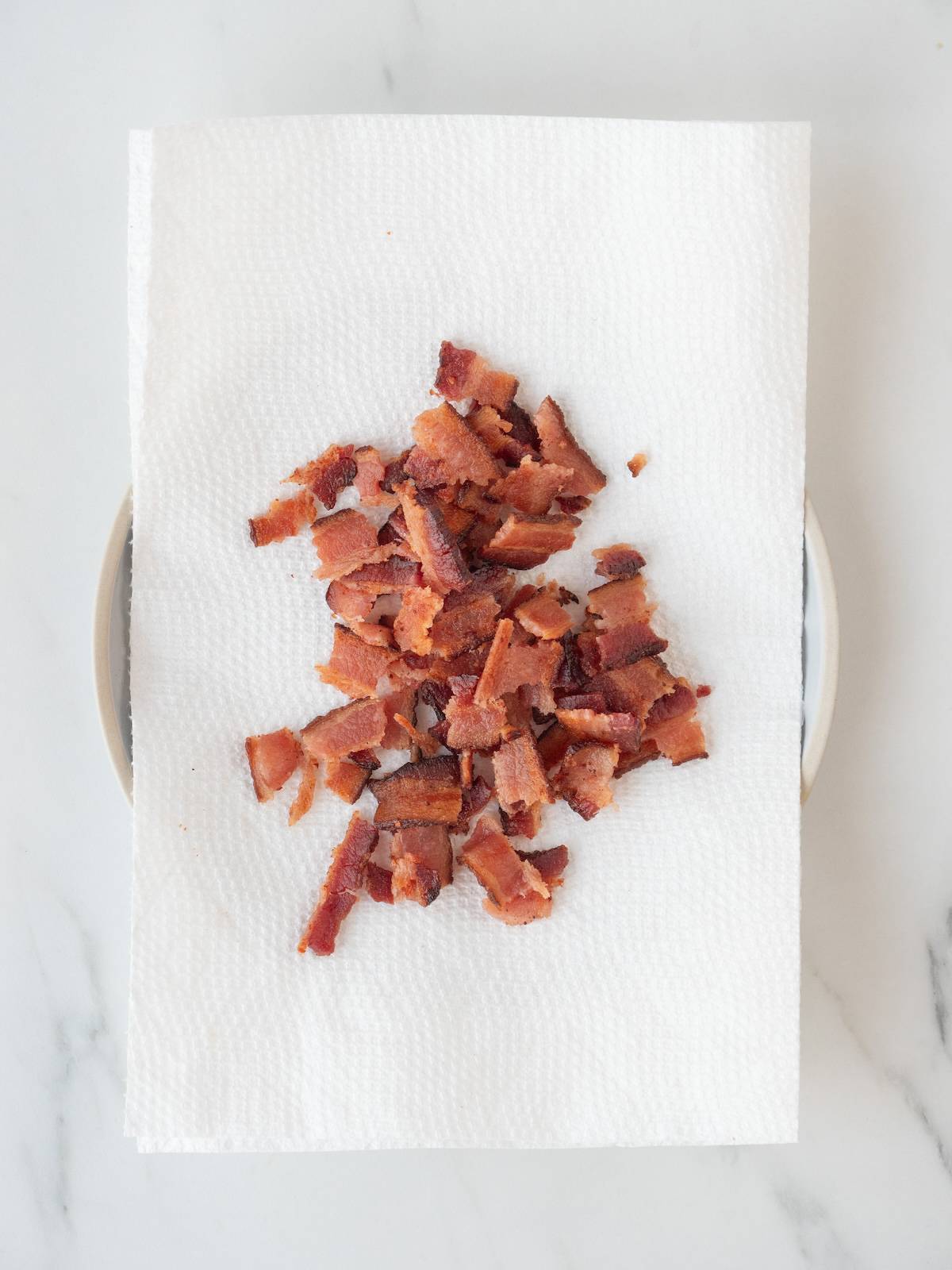 A tissue lined plate with cooked bacon, broken into bite sized pieces.