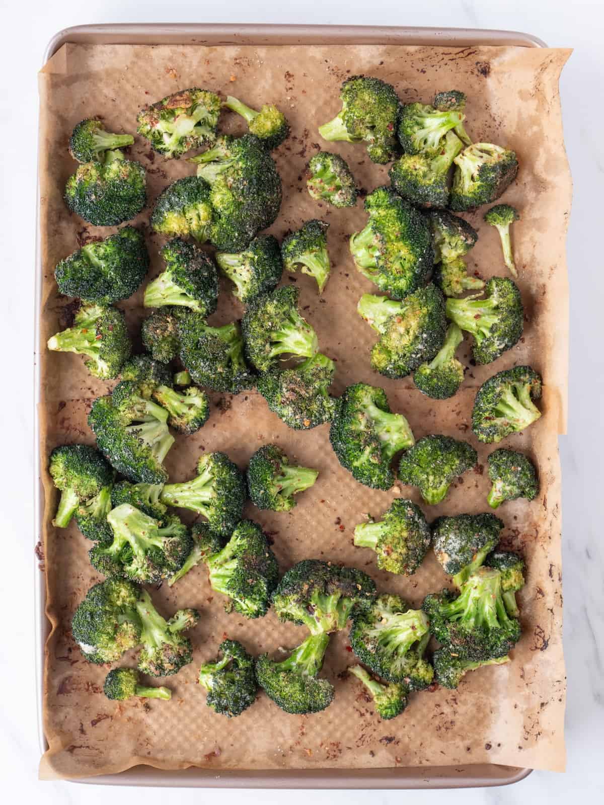 A parchment-lined baking sheet with broccoli florets baked, crispy and just out of the oven.