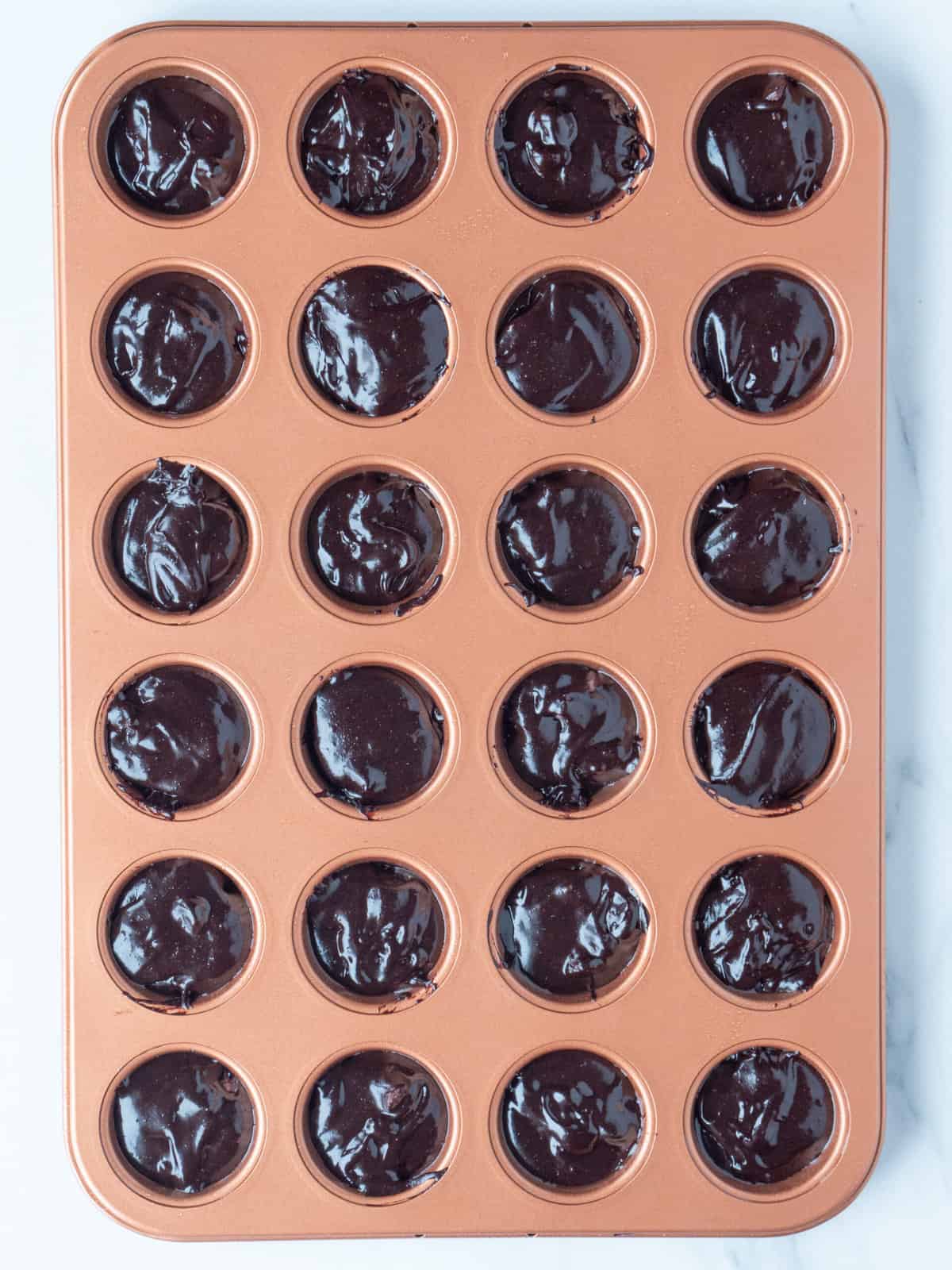 A 4x6 mini cupcake pan with brownie mixture scooped into it.
