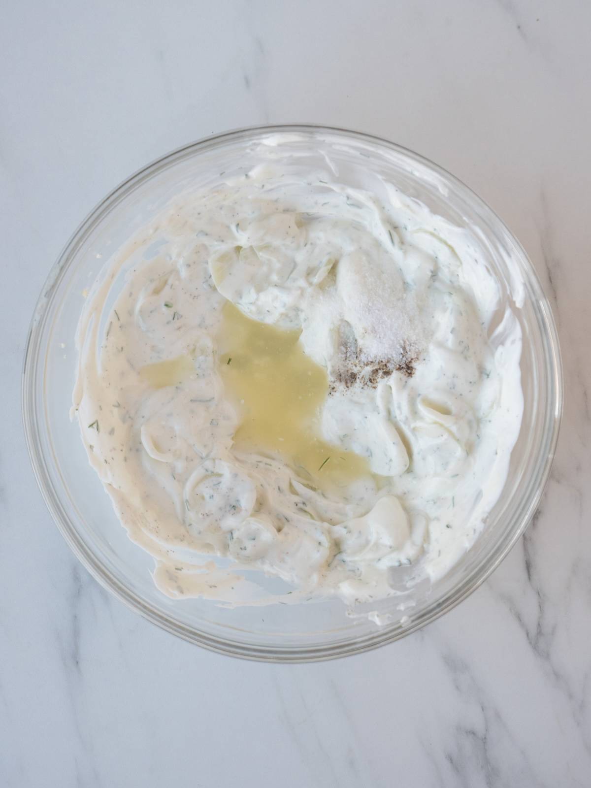 A glass mixing bowl with tzatziki, topped with lemon juice.
