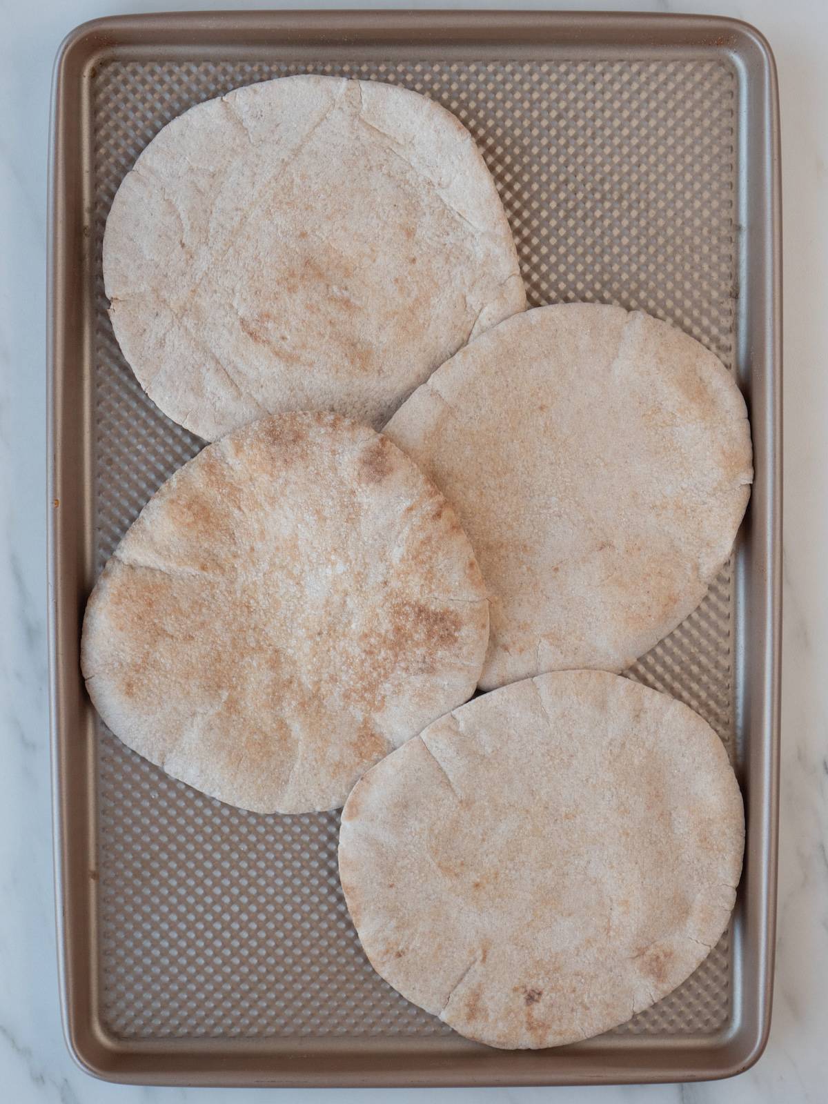 A baking sheet with whole wheat pitas laid out, slightly overlapping each other.
