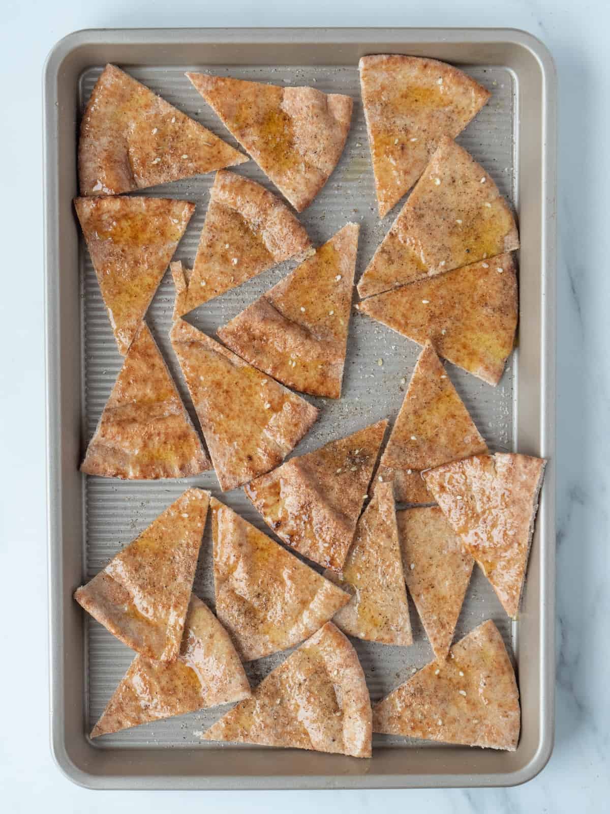 A baking sheet with pitas sliced into wedges, brushed with olive oil and sprinkled with the za'atar-salt mixture.