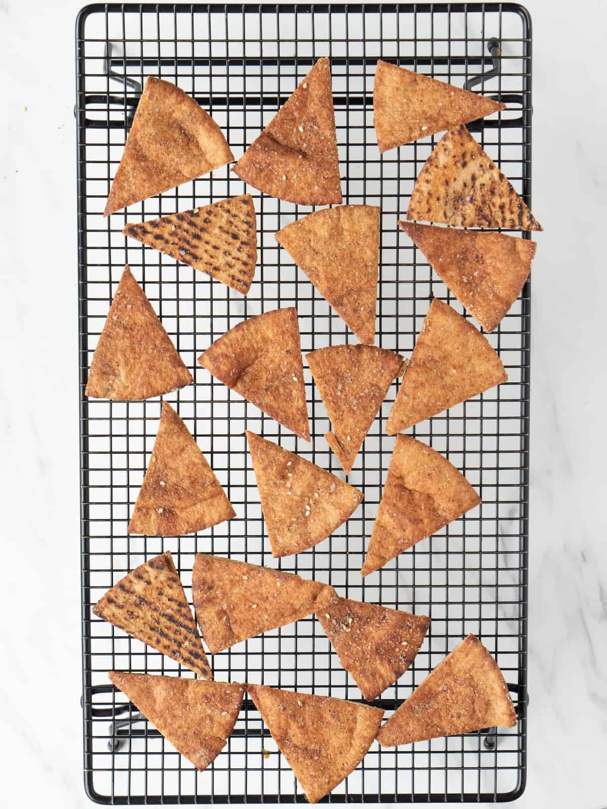 A wire rack with pita wedges baked into chips, fresh out of the oven being cooled on the rack.