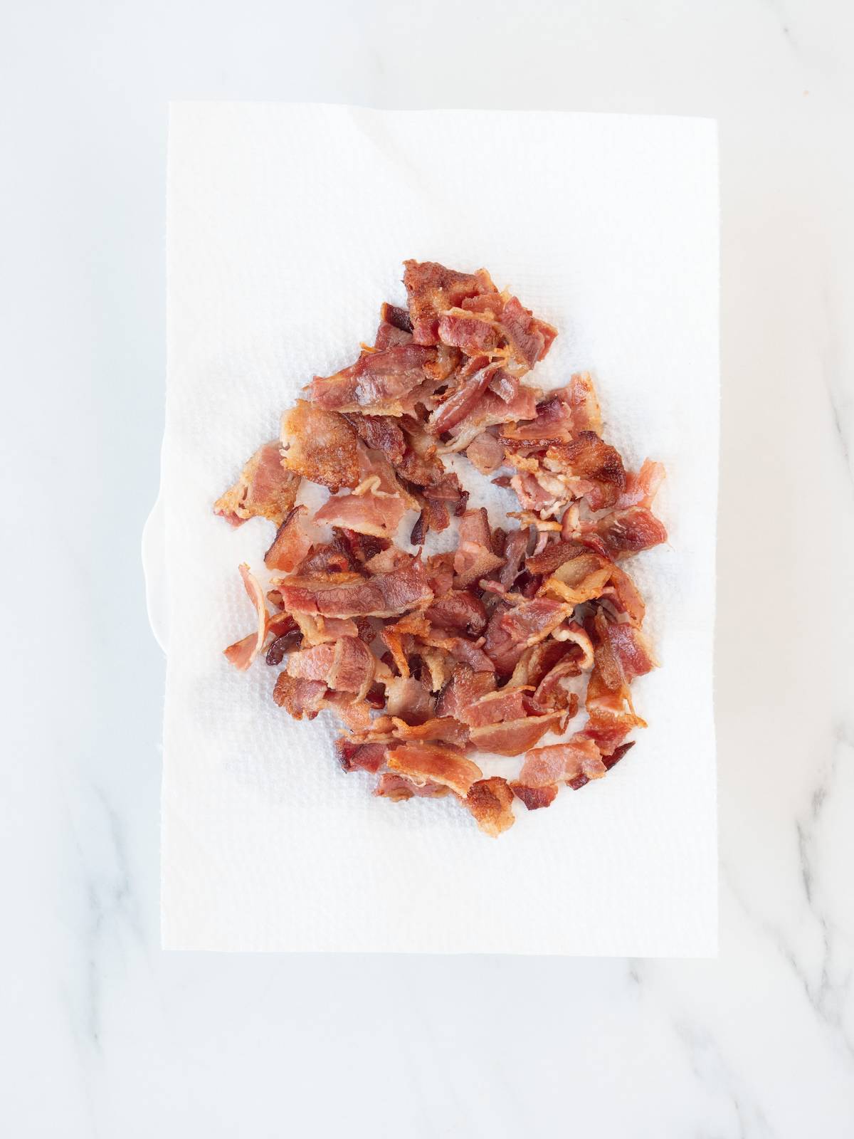 A tissue paper laid out on the kitchen counter, with cooked bacon on it that has been torn into small pieces.