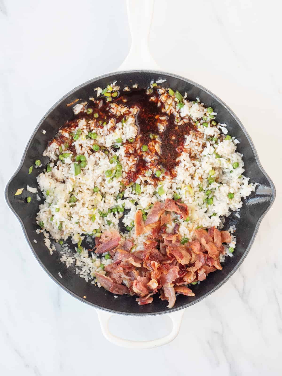 A skillet with rice being sautéed, and bacon bits and soy sauce-sambal mix just added.