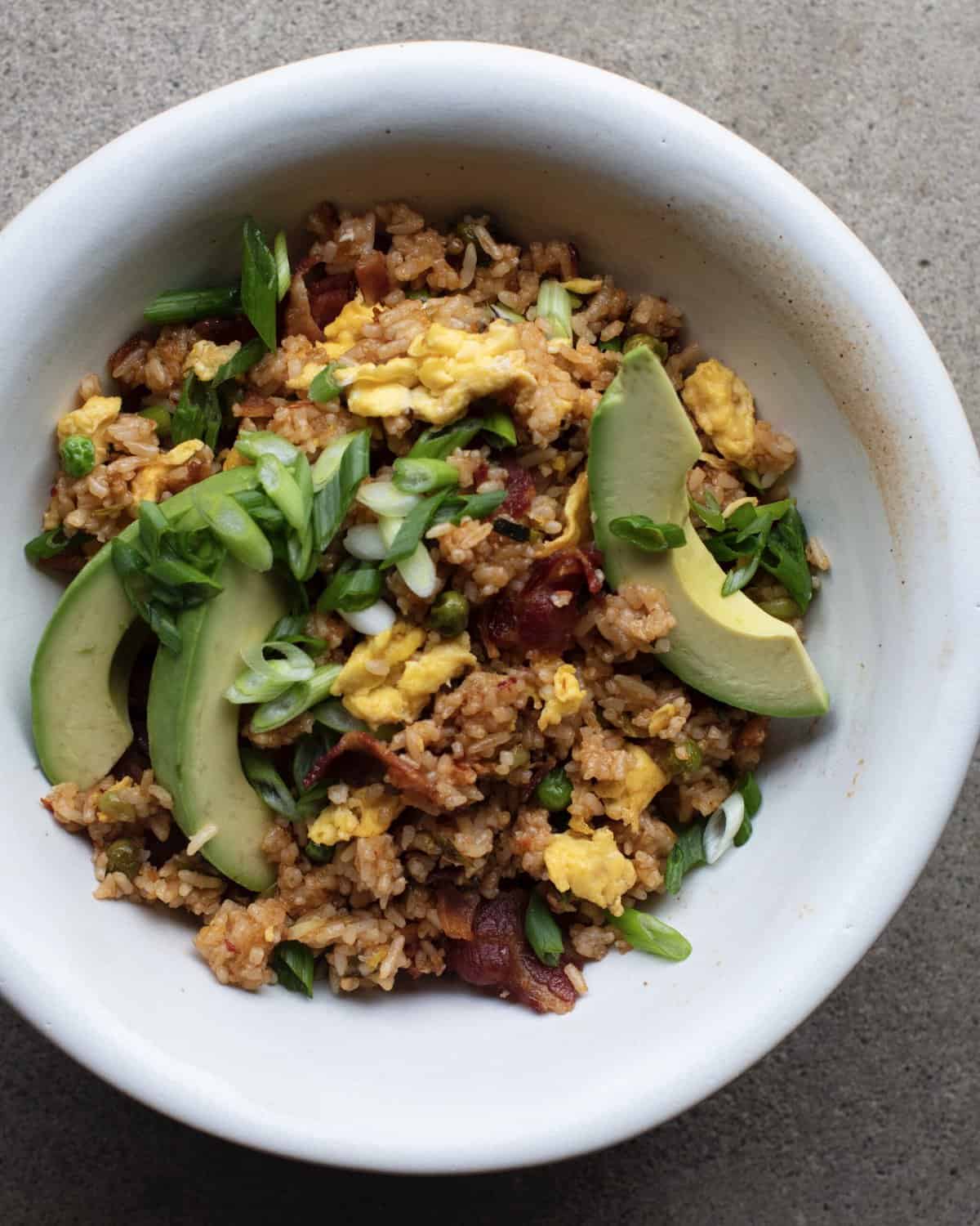 A bowl with spicy bacon fried rice, topped with avocado wedges.