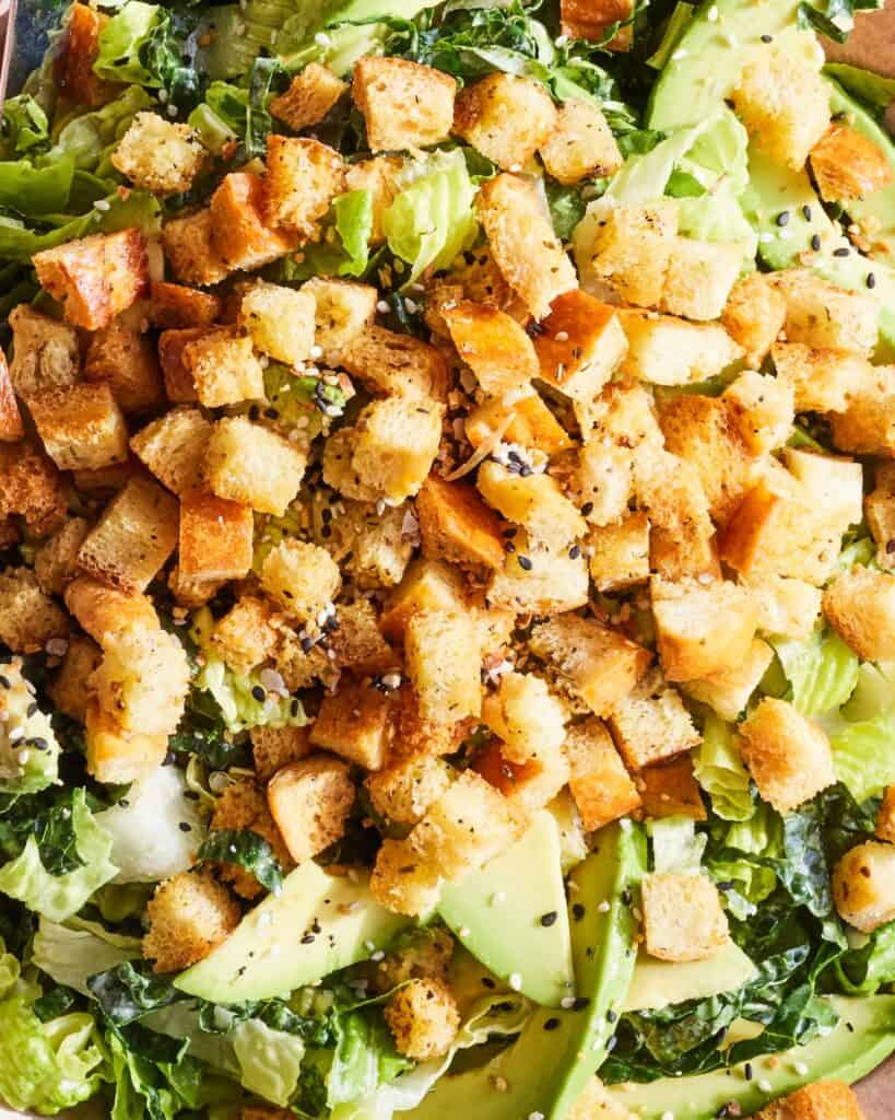 An overhead close up shot of avocado kale caesar salad, with croutons on top.