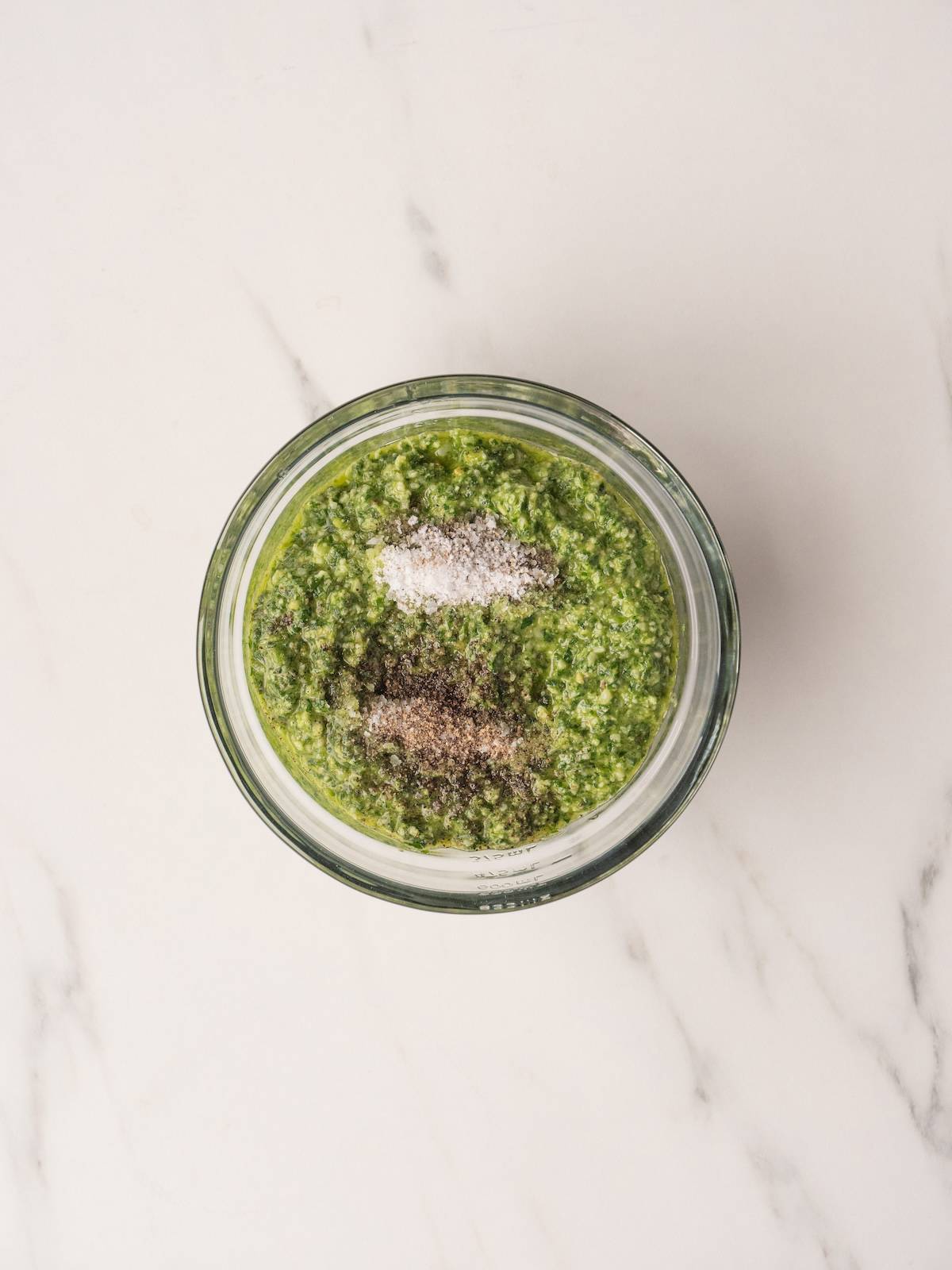A glass bowl with arugula pesto to which salt and pepper has been added.
