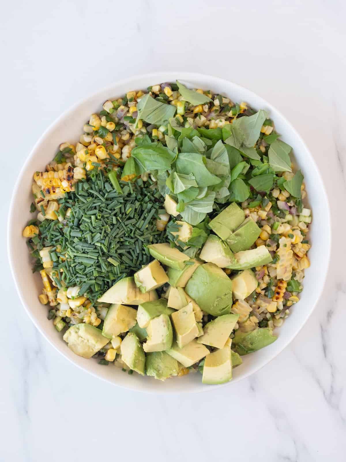A bowl with avocado corn salad, topped with chopped chives, basil and avocado.