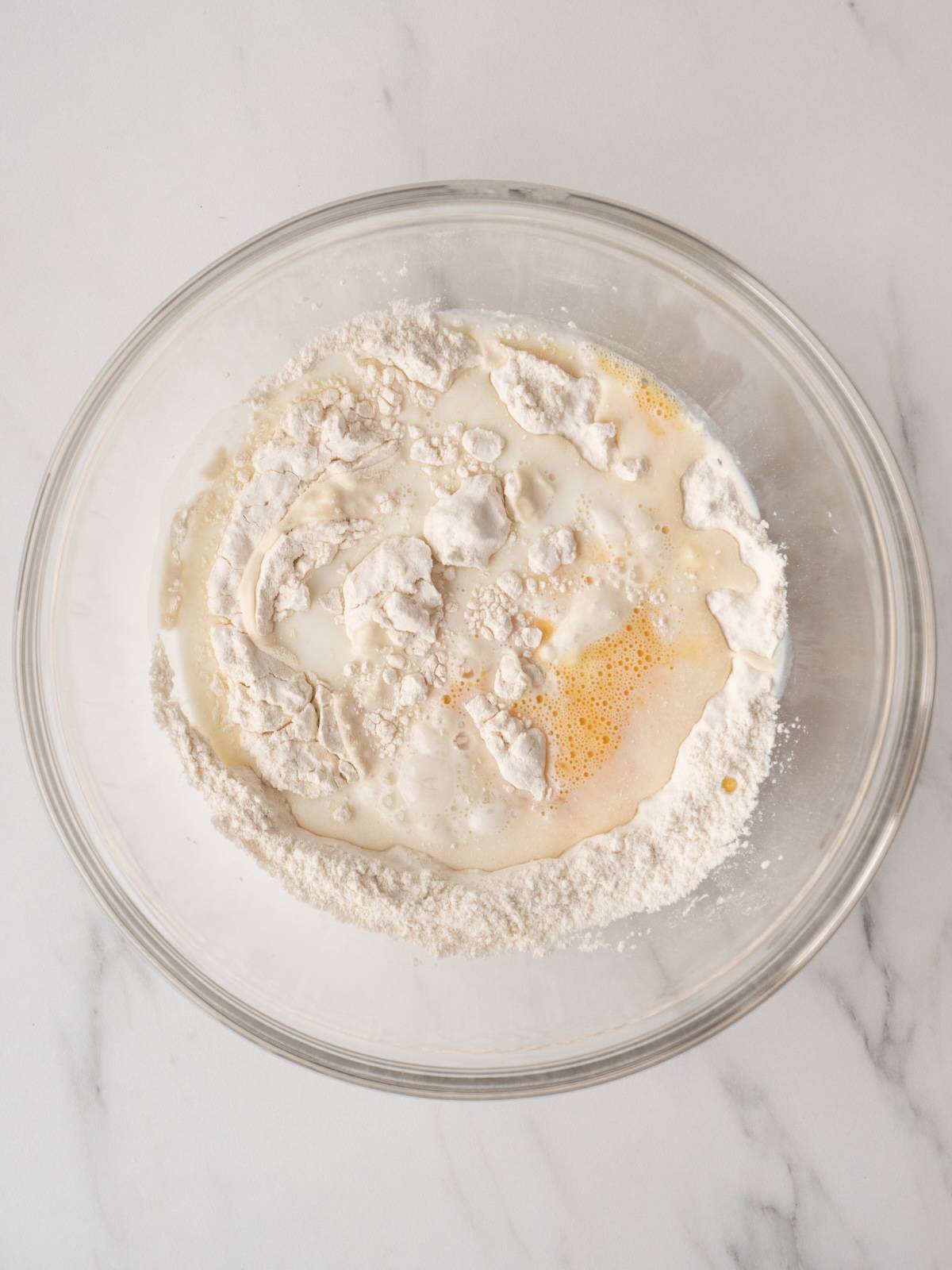 A large glass mixing bowl with flour and baking powder mix, with milk and egg added.