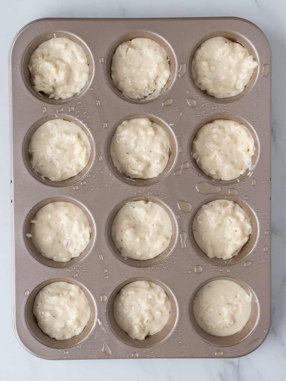 A 12 muffin pan with pizza bites batter added to each of the muffin cups.