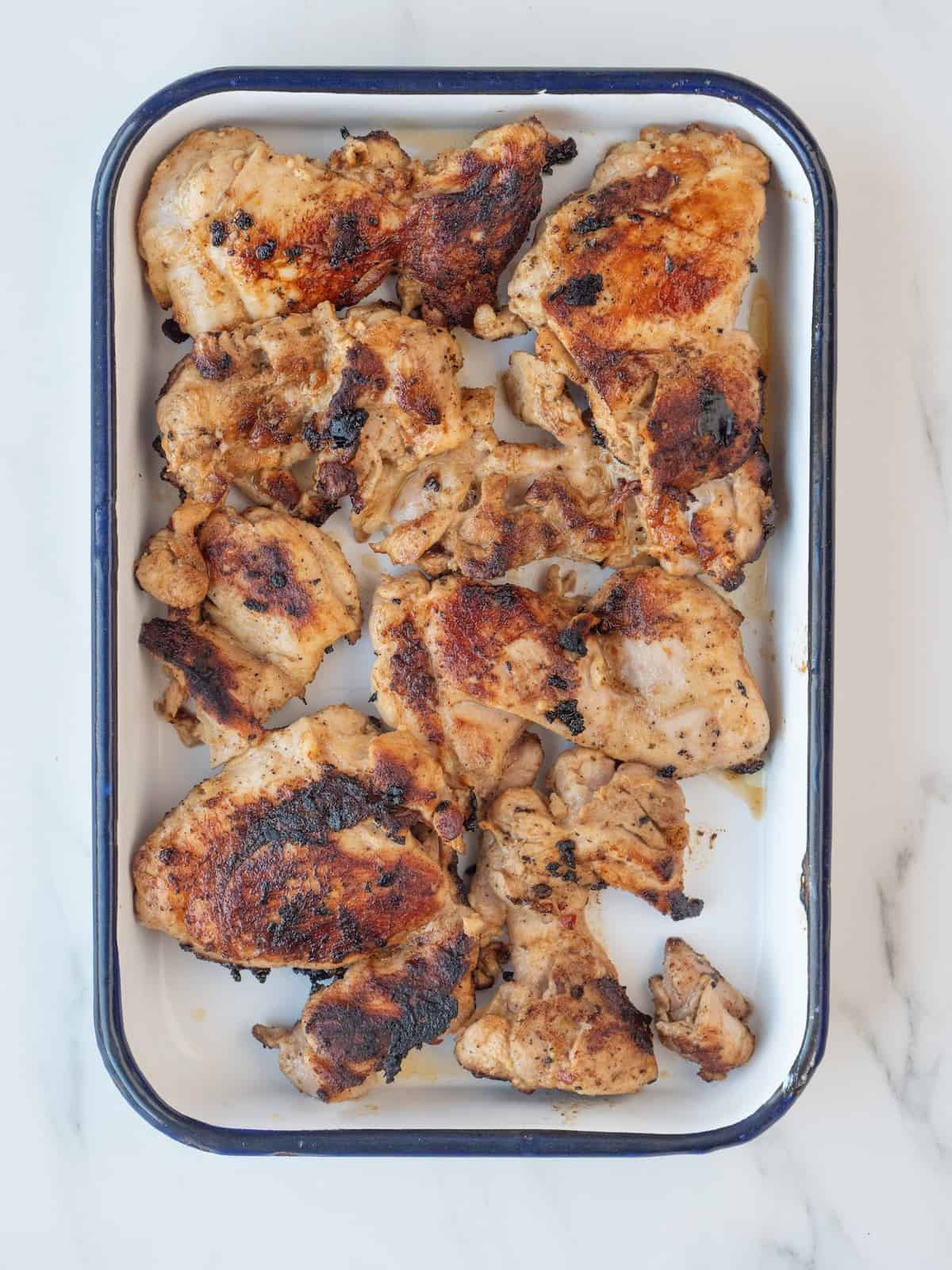 A rectangular dish with grilled chicken thighs resting after being grilled on a cast iron.