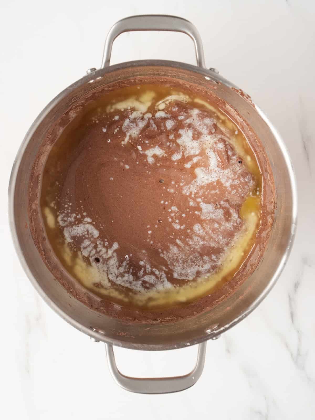 A stand mixer bowl with beaten eggs, sugar and dry ingredients mixed together to make chocolate brownie pudding and cooled melted butter just added.