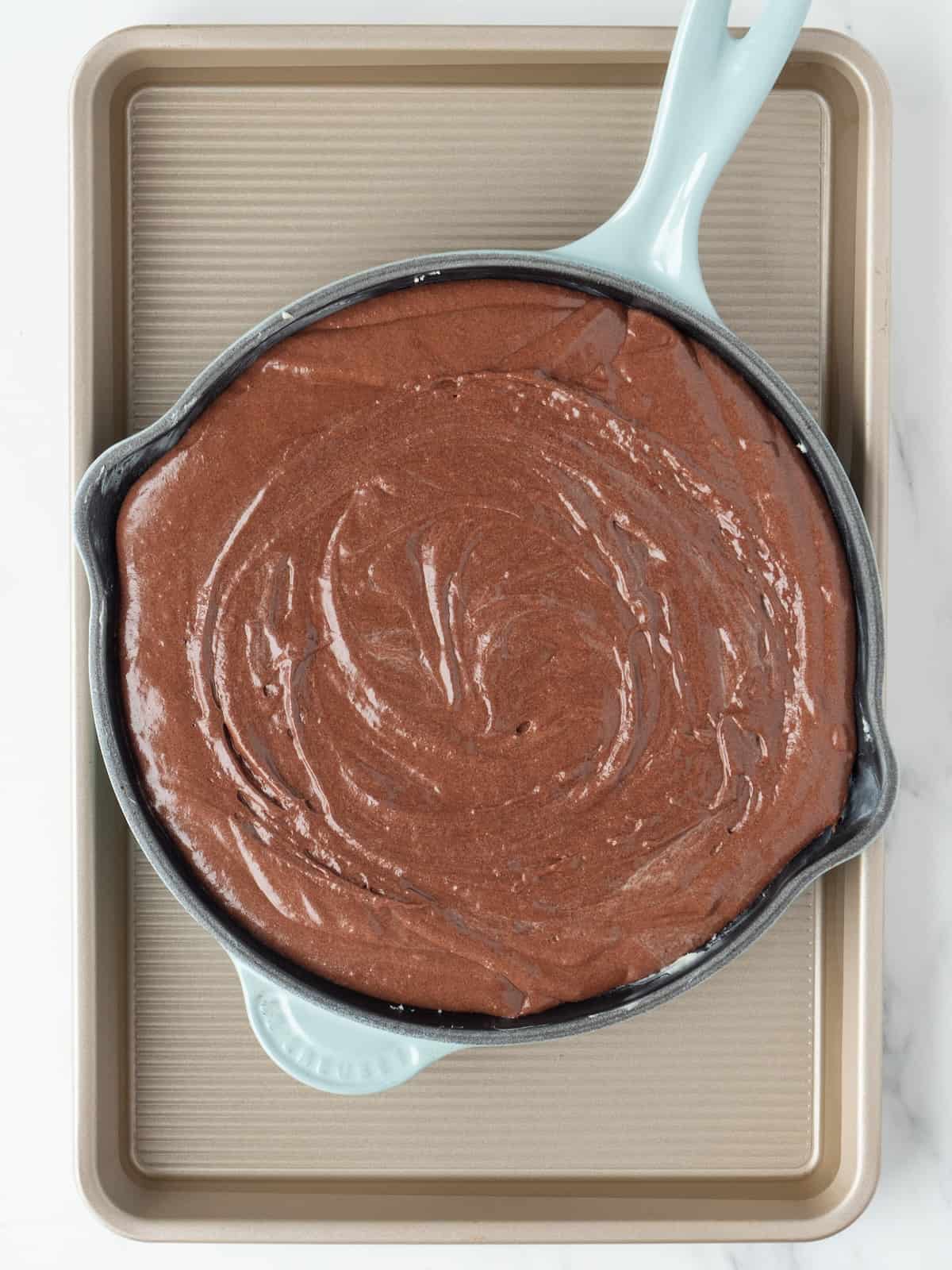 A 9 inch skillet with chocolate brownie pudding batter, placed in a larger baking pan with hot water coming halfway up the side of the skillet.