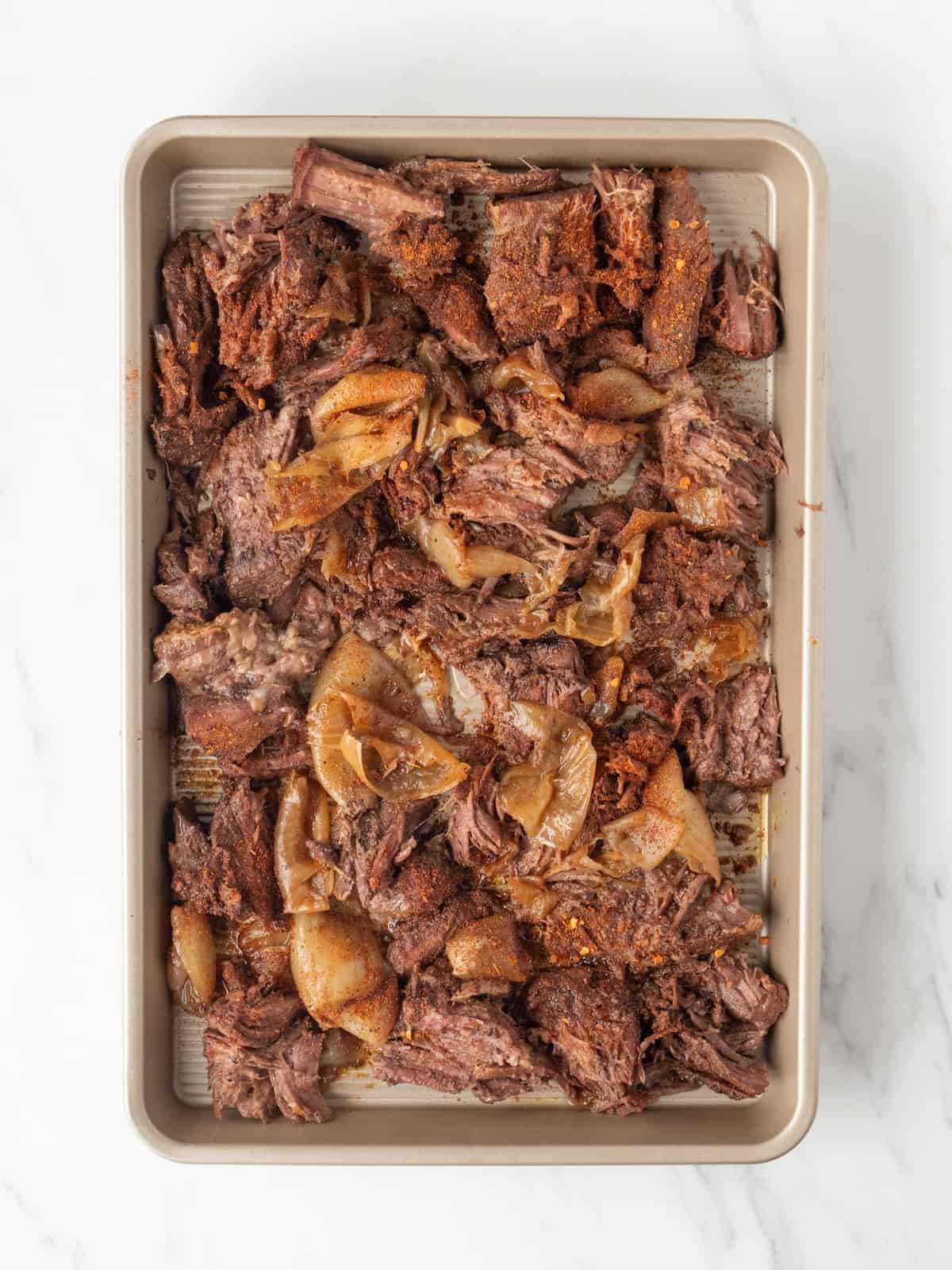A baking sheet with shredded cooked chuck roast, and onions it cooked with.