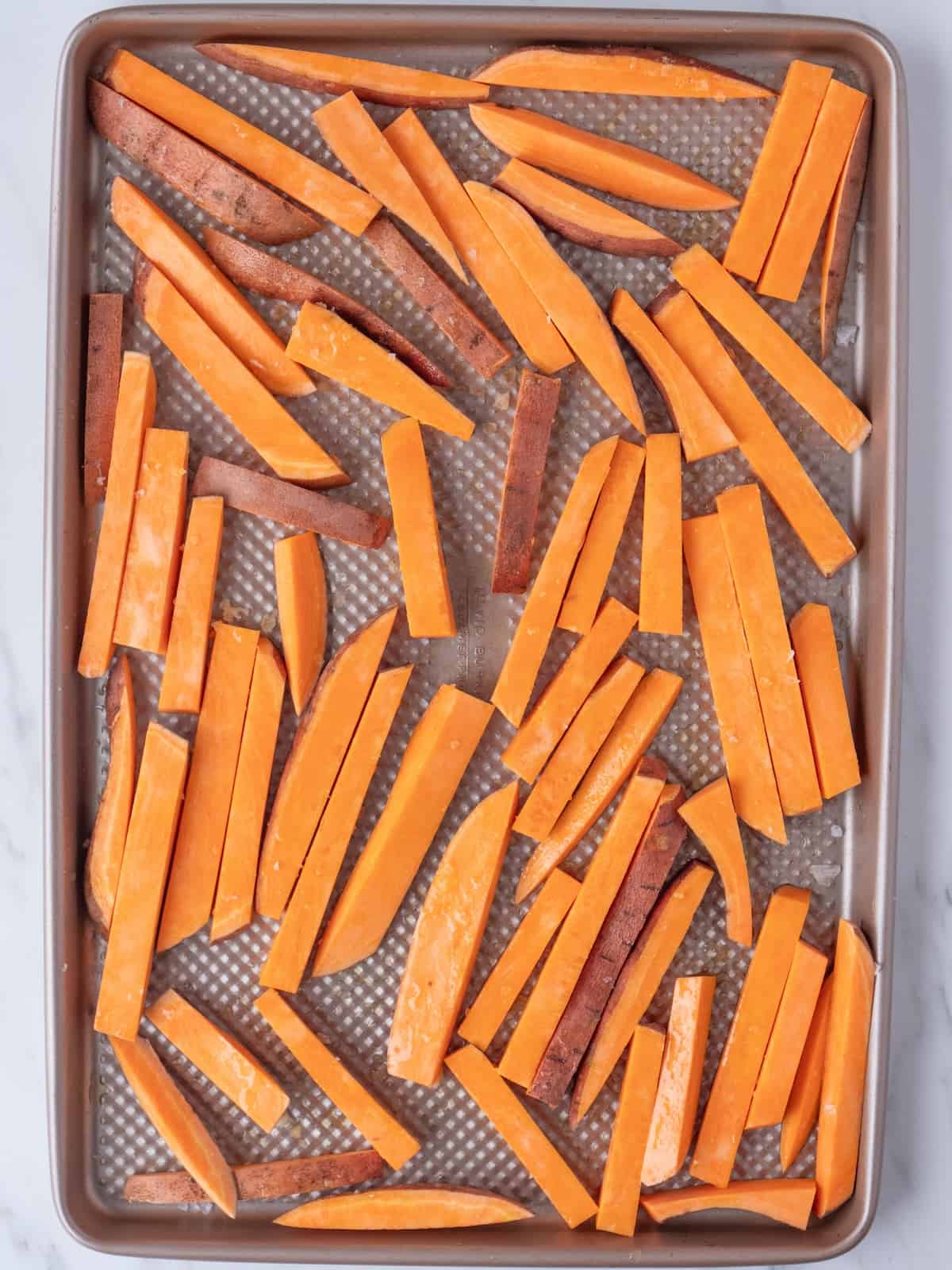 A baking sheet with unpeeled sweet potatoes cut length wise into batons about ¼ inch wide and 3 inches long.