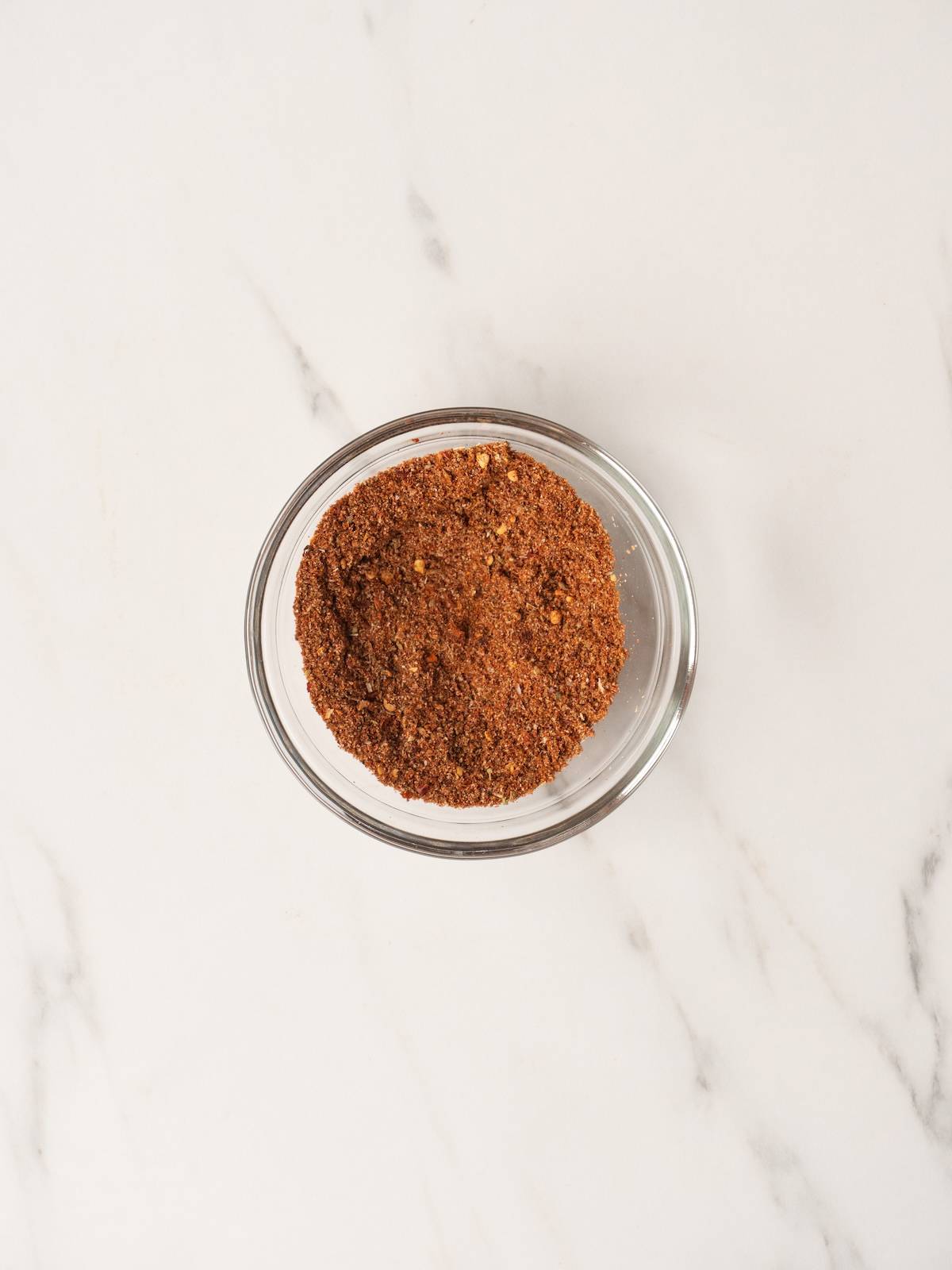 A small glass mixing bowl with all the eight spices mixed together to make homemade taco seasoning. 